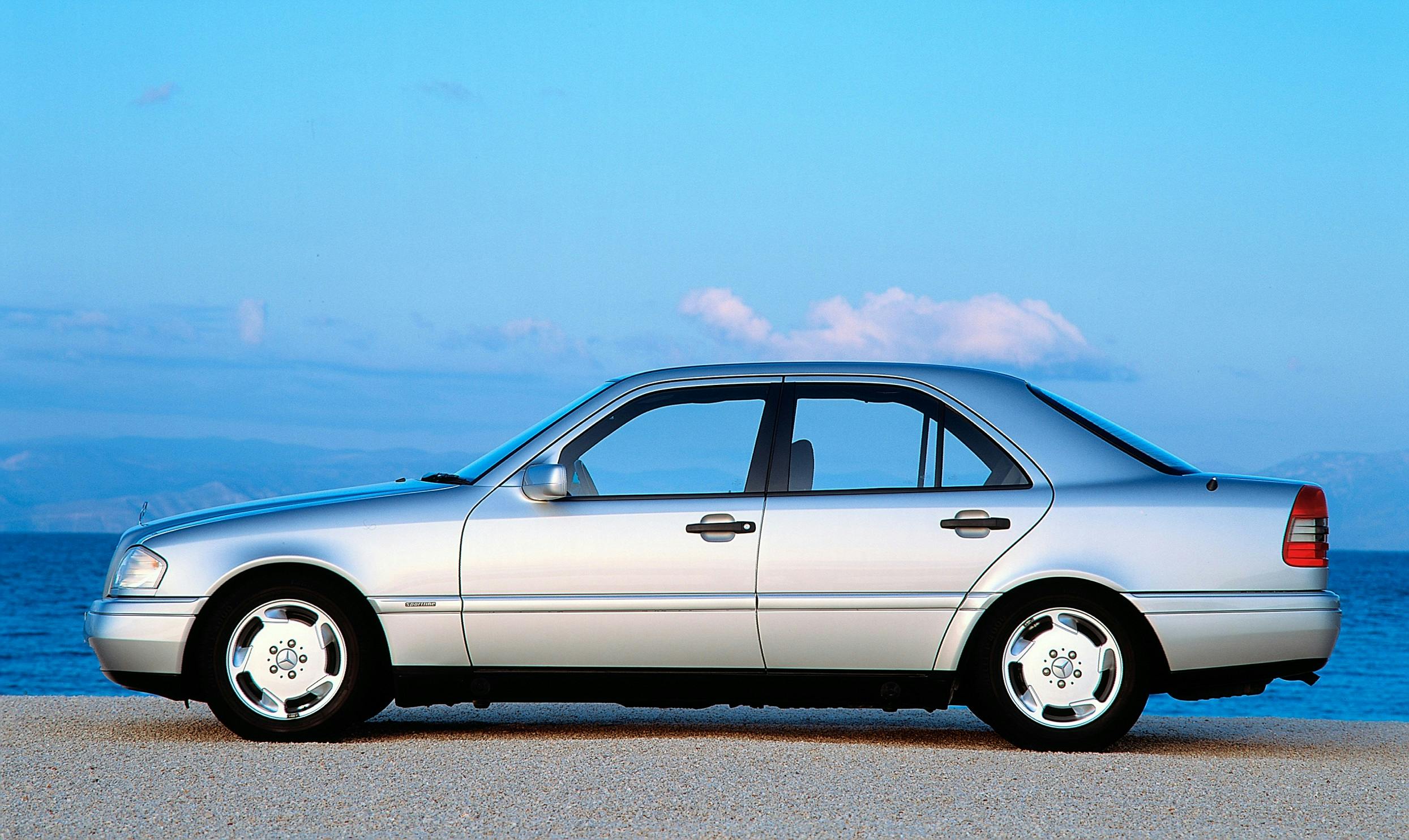 Silberner Pkw, seitlich fotografiert, steht auf sandigem Untergrund vor blauem Himmel und Meer im Hintergrund.