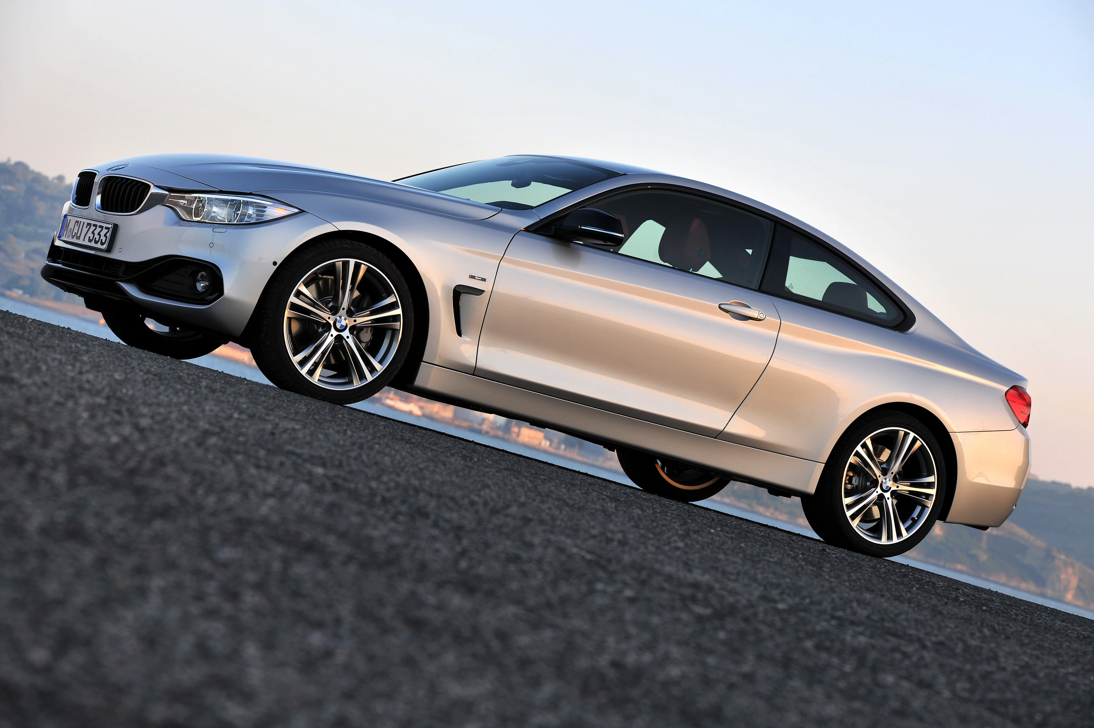 Silbernes BMW-Coupé steht seitlich auf Asphaltstraße, leichter Aufwärtswinkel, mit blauem Himmel im Hintergrund.