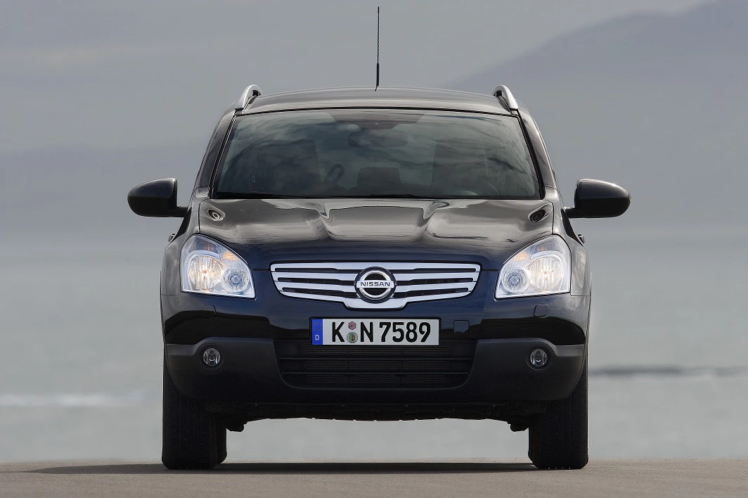 Schwarzer Nissan Qashqai aus Vorderansicht, Scheinwerfer eingeschaltet, vor verschwommenem Hintergrund.