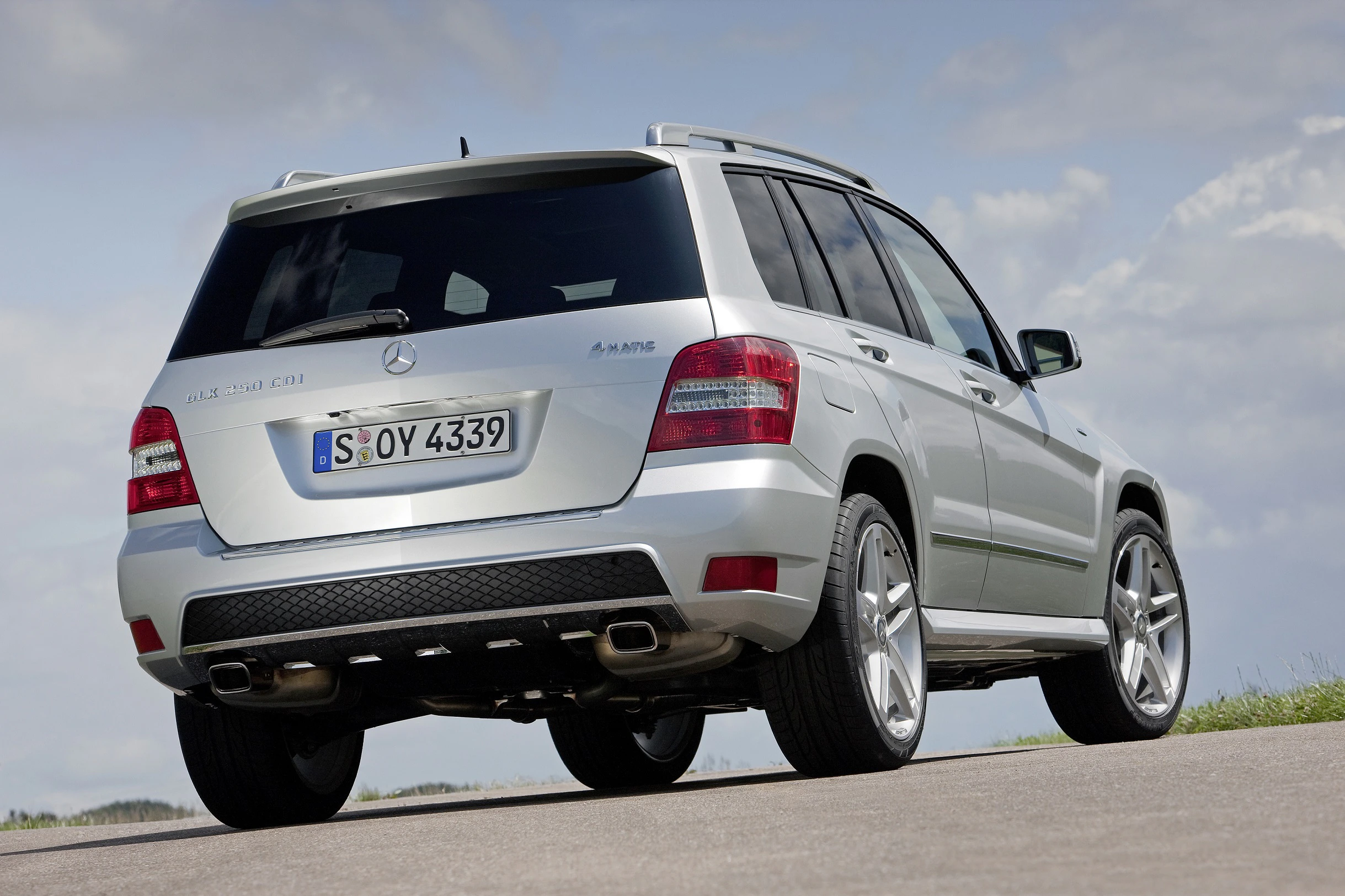 Silberner Mercedes-Benz SUV auf einer Straße, Rückansicht. Sonniger Himmel im Hintergrund.