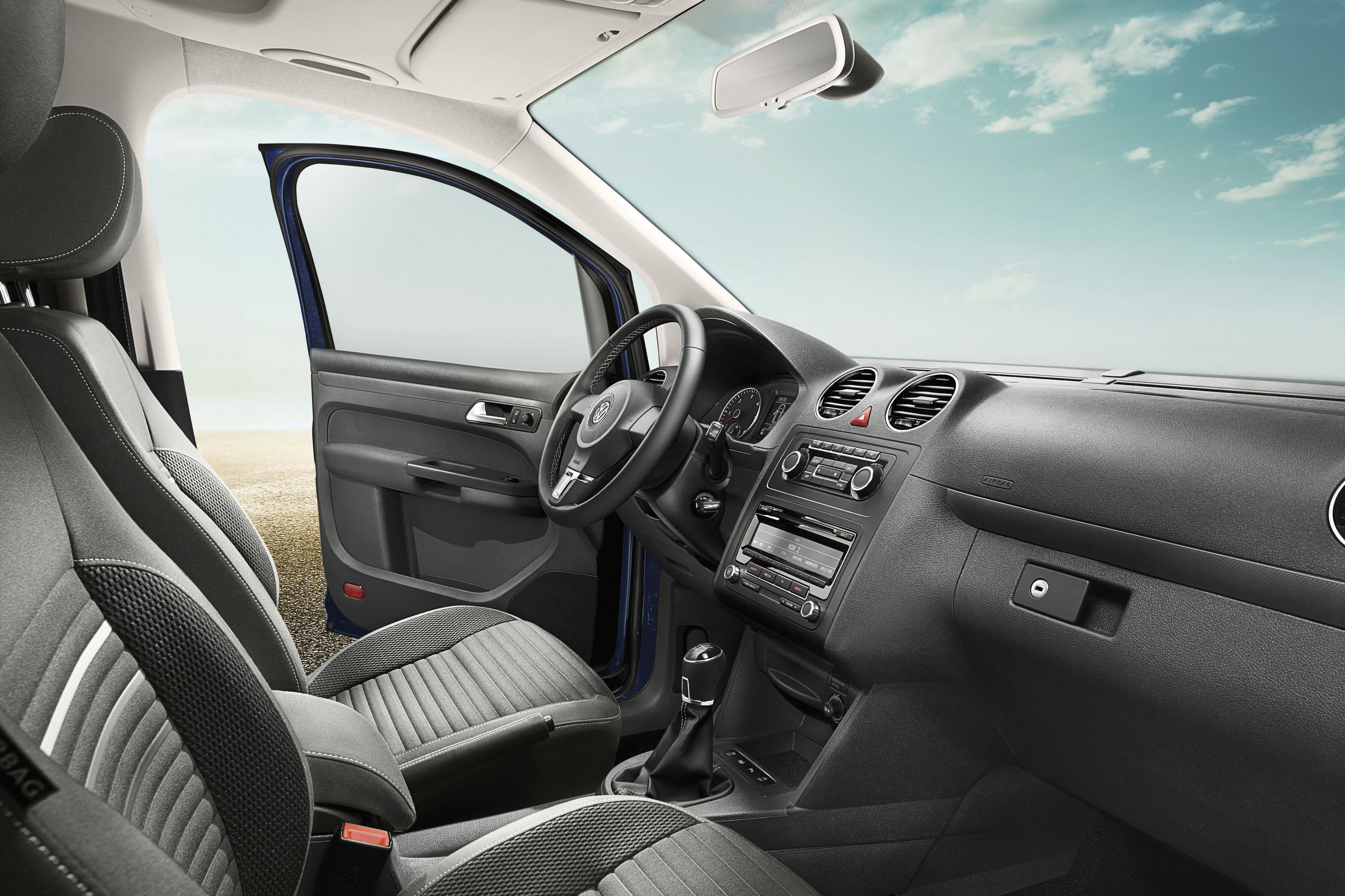 Innenraum eines Autos mit geöffnetem Fahrertür. Ledersitze, Lenkrad, Amaturenbrett und Schalthebel sind sichtbar. Heller Himmel im Hintergrund.