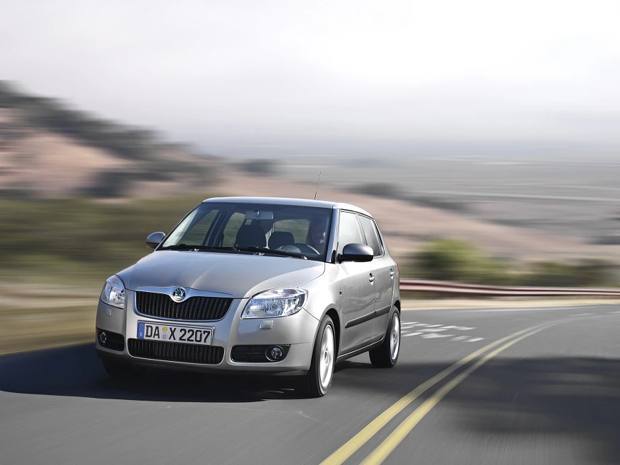 Silberner Skoda Fabia fährt auf einer kurvigen Landstraße, unscharfer Hintergrund zeigt Landschaft und Bewegung.