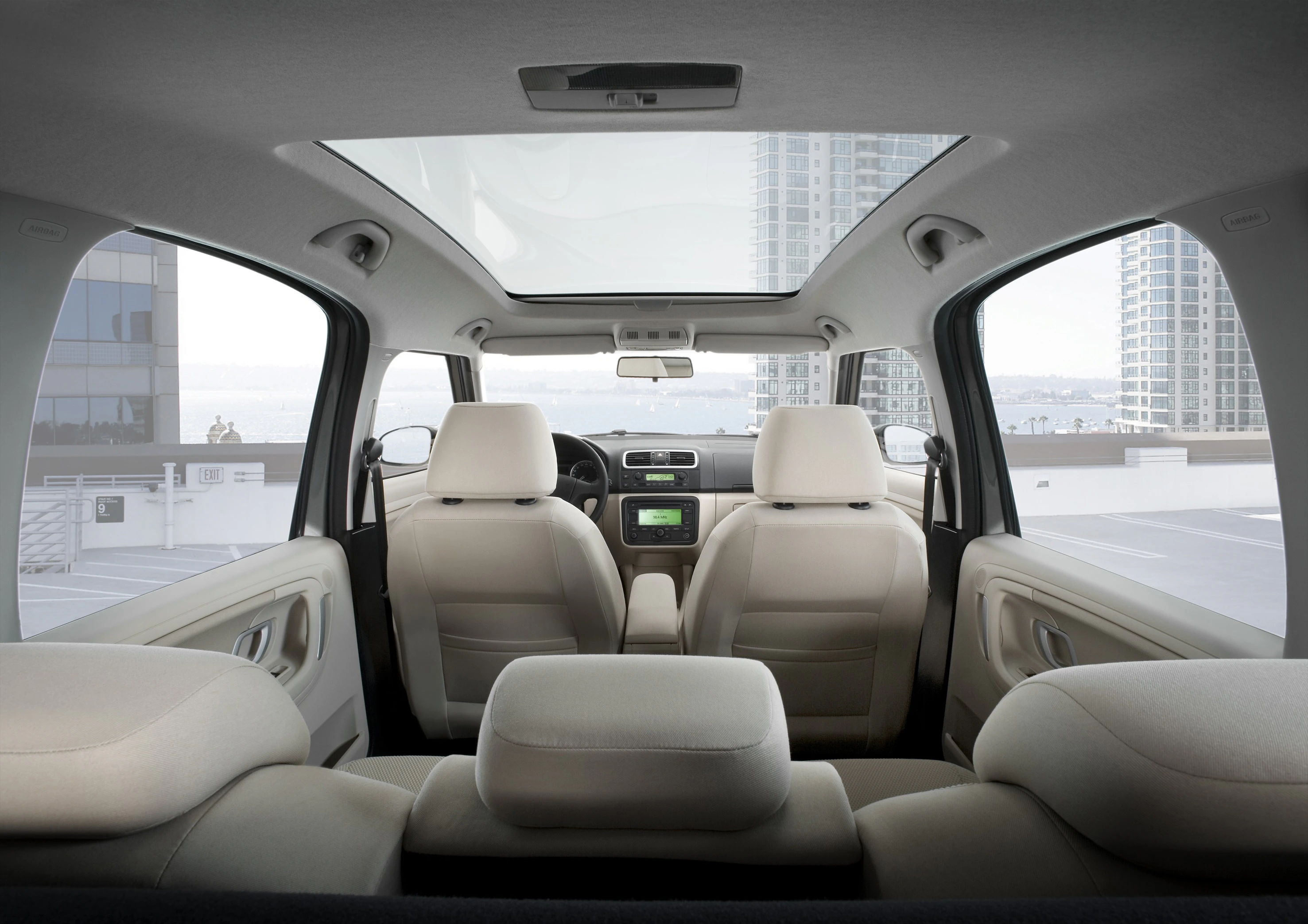 Innenansicht eines modernen Autos mit beigen Sitzen und Panoramaschiebedach, geparkt auf einem städtischen Dach mit Blick auf hohe Gebäude.