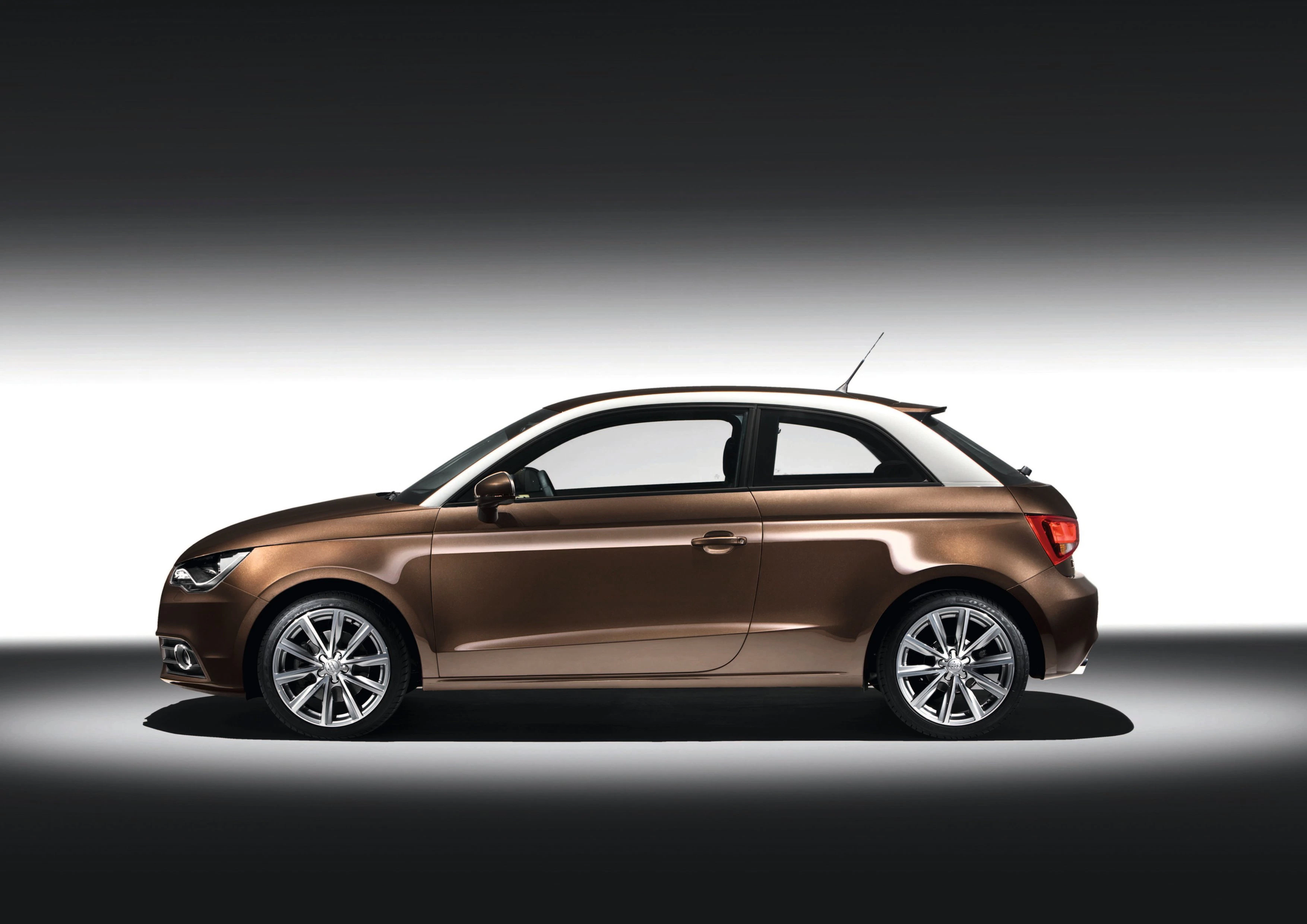 Kompaktes, dreitüriges Auto in metallischem Bronze, seitlich fotografiert, auf grauem Hintergrund mit sanftem Licht.