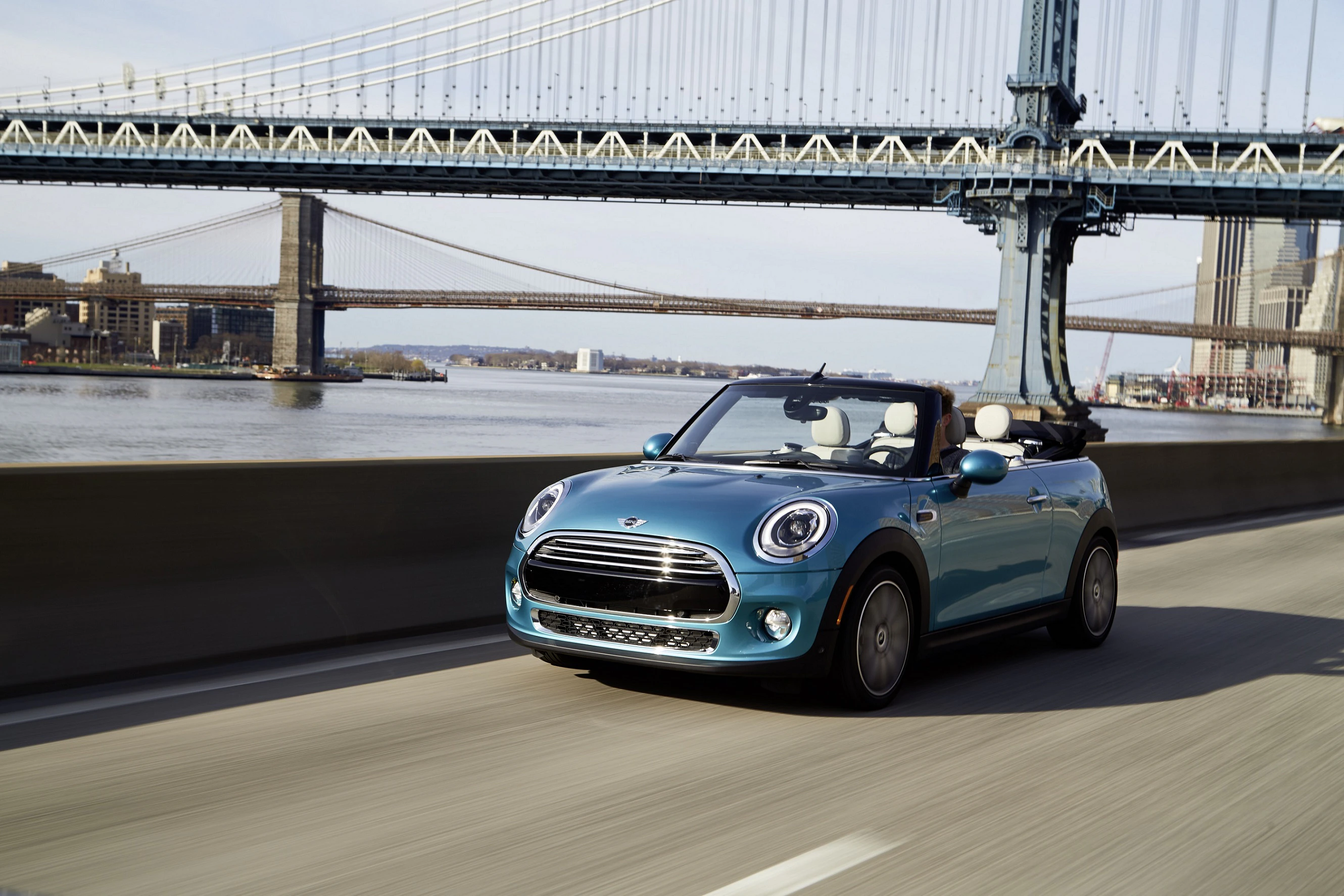 Blauer Cabrio-Mini fährt auf einer Brücke mit Fluss und zweiter Brücke im Hintergrund an einem sonnigen Tag.