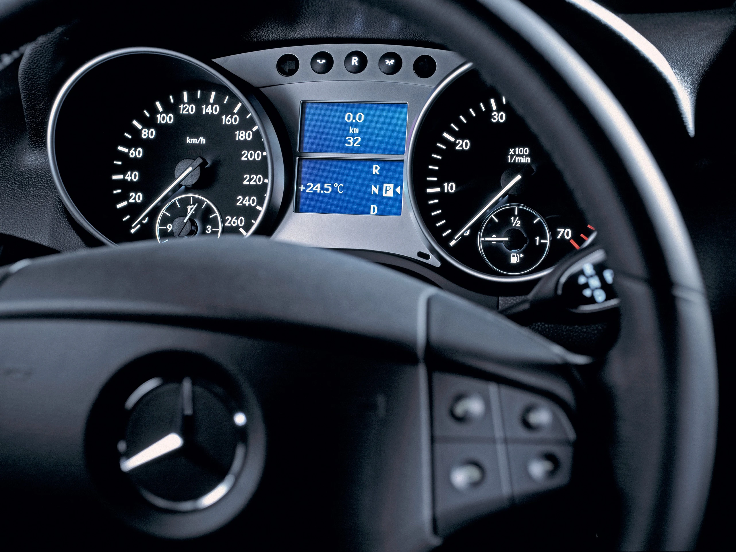 Nahaufnahme eines Mercedes-Benz Armaturenbretts mit Geschwindigkeits- und Drehzahlanzeige, Lenkrad mit Logo im Vordergrund.