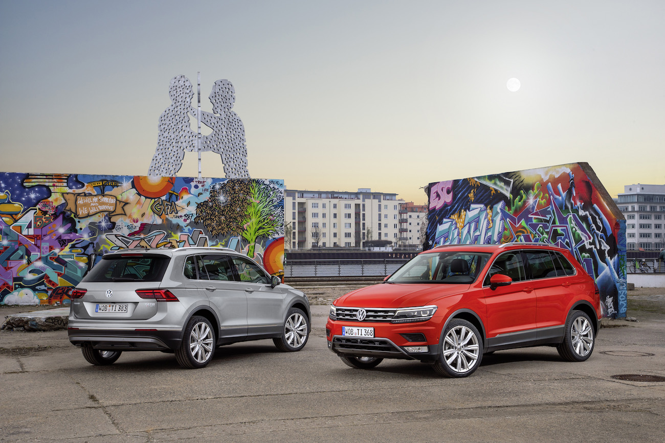 Zwei VW Tiguan Autos, eines silbern und eines rot, stehen vor bunten Graffiti-Wänden und einer modernen Skulptur in urbaner Umgebung.