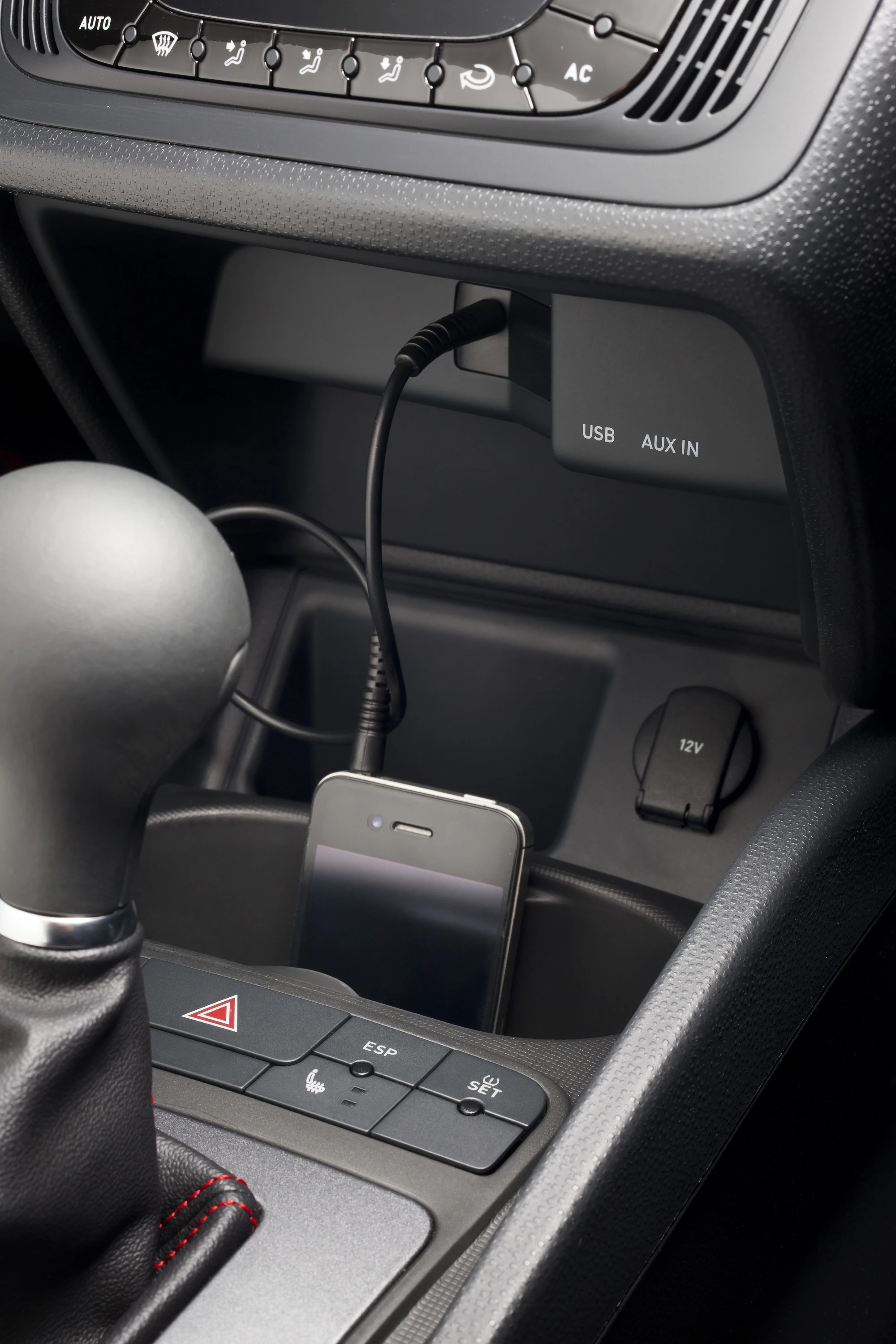 Smartphone im Auto am USB-Anschluss aufgeladen, neben Schalthebel und Bedienknöpfen.