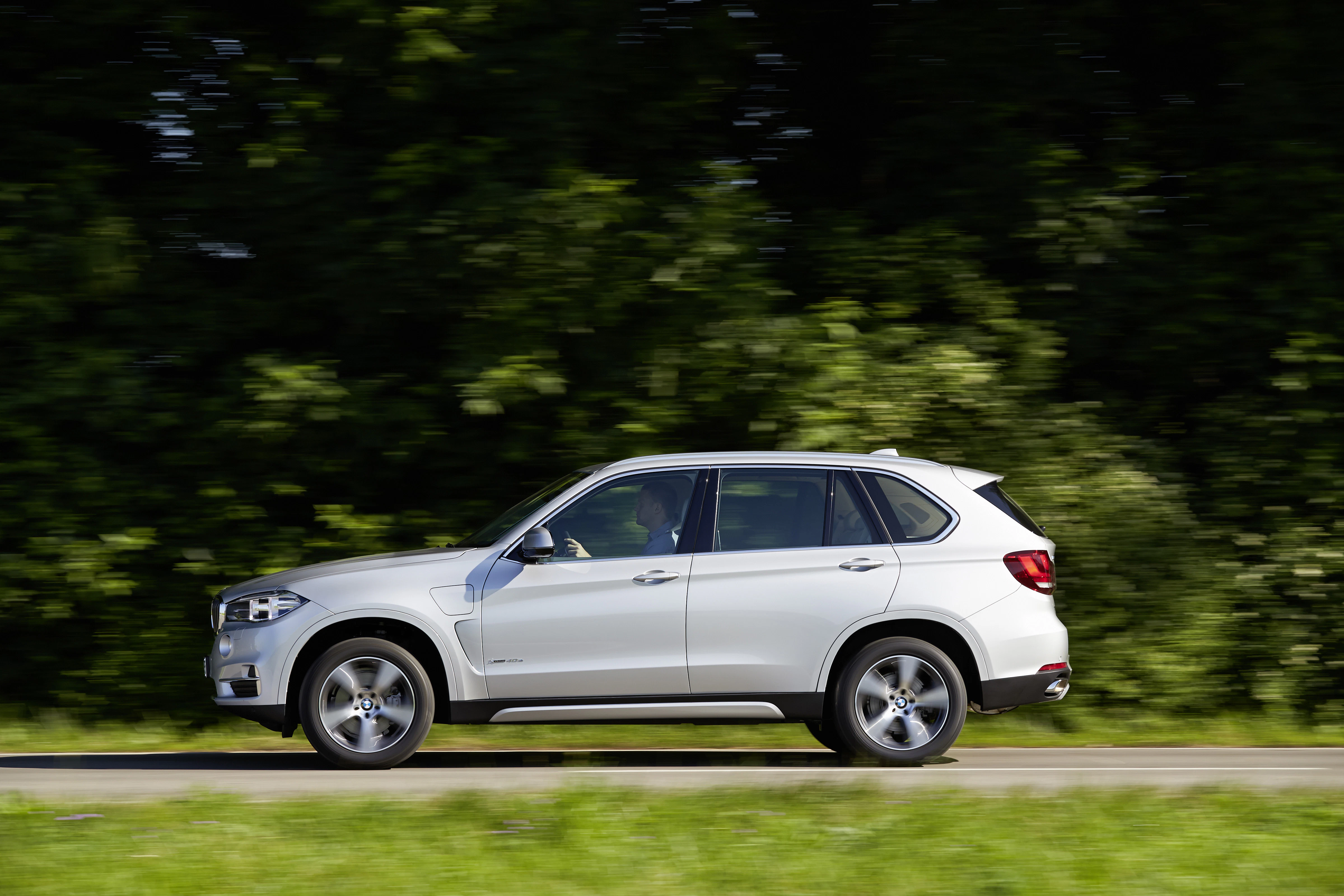 Weißes SUV fährt auf einer Landstraße vor einer grünen Baumkulisse.