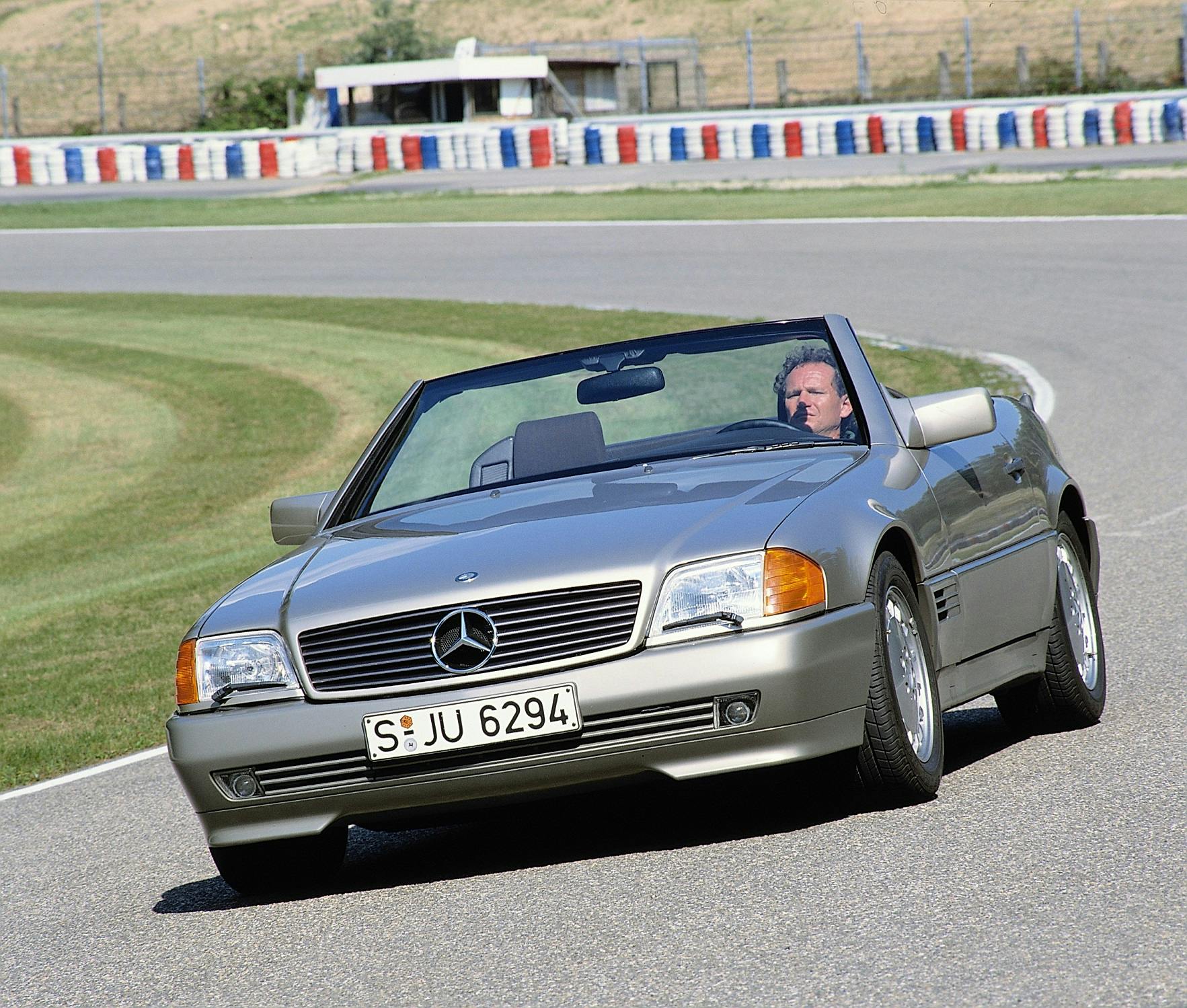 Graues Mercedes-Cabrio fährt auf Rennstrecke. Einzelner Fahrer am Steuer, keine weiteren Fahrzeuge in Sicht, klare Wetterbedingungen.