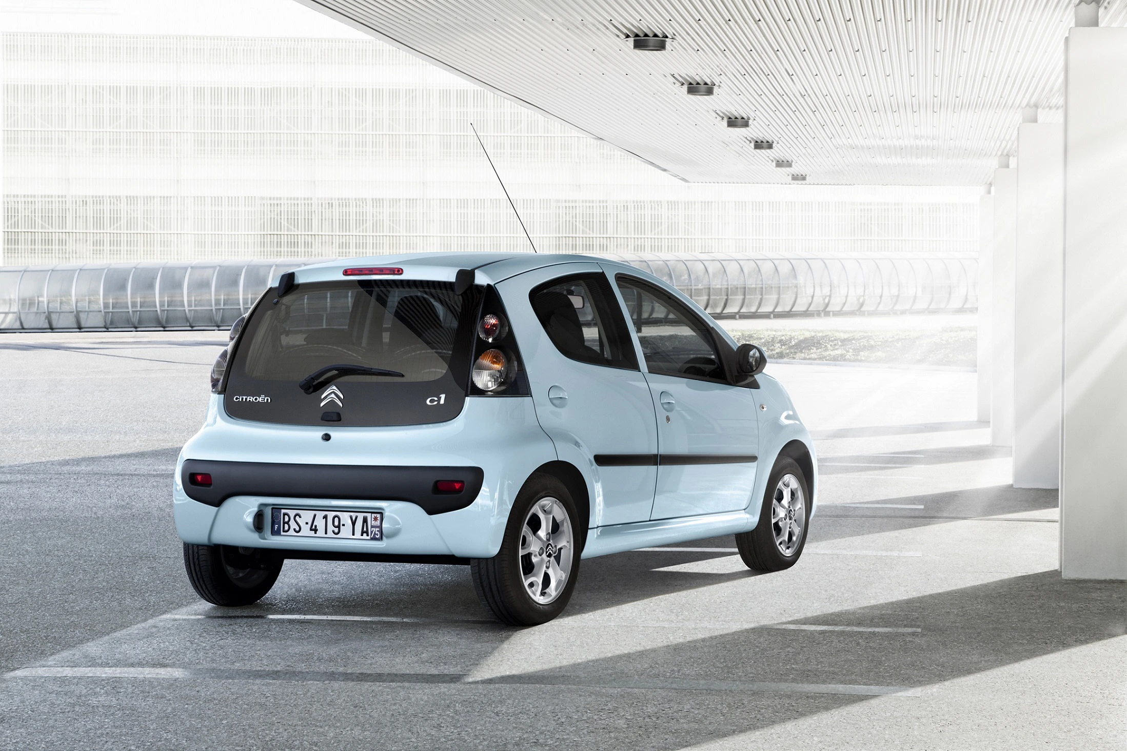 Kleiner, hellblauer Citroën C1 steht in einem modernen, überdachten Bereich mit indirektem Sonnenlicht im Hintergrund.