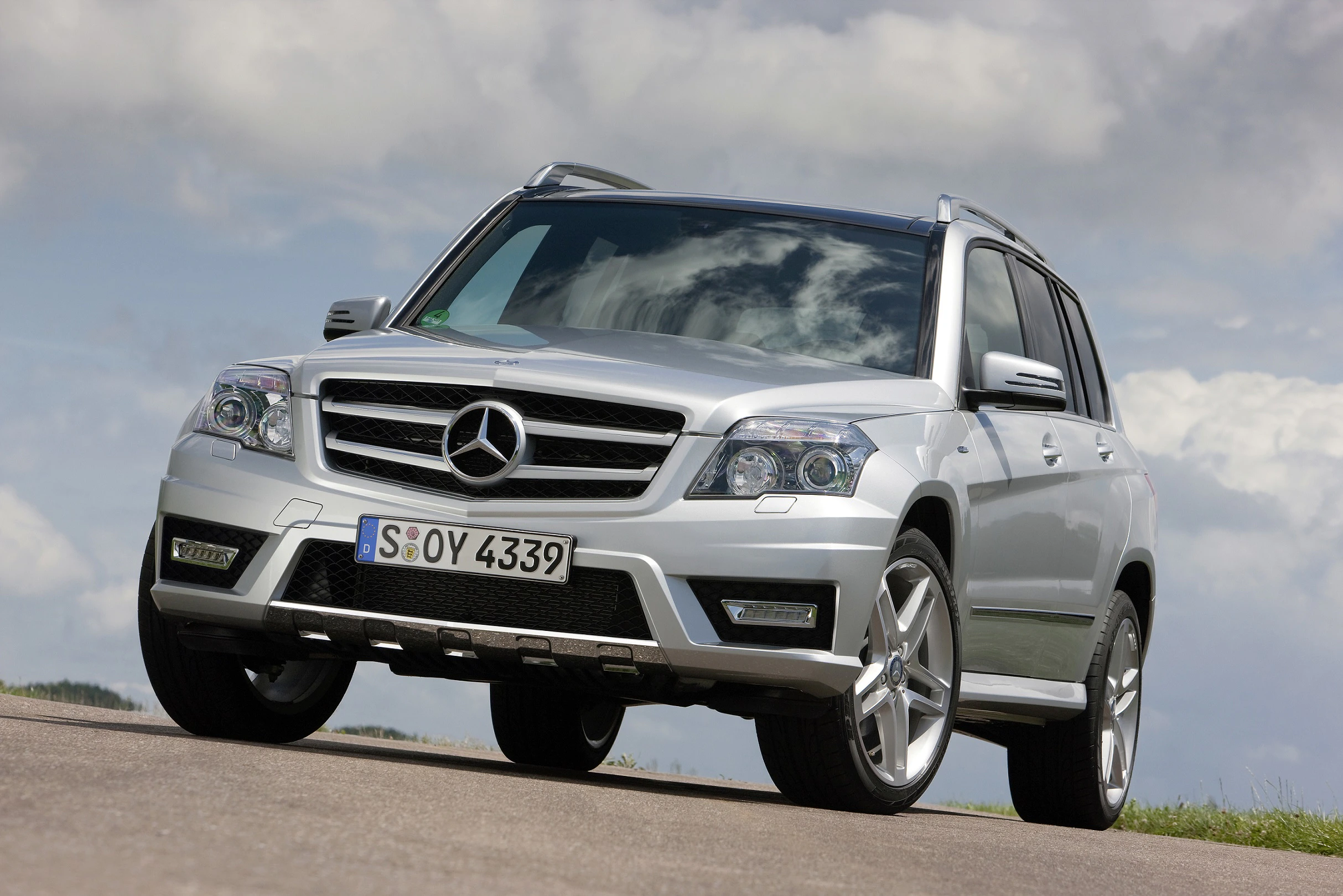 Silberner Mercedes-Benz SUV parkt auf einer malerischen Straße, mit Wolkenhimmel im Hintergrund.