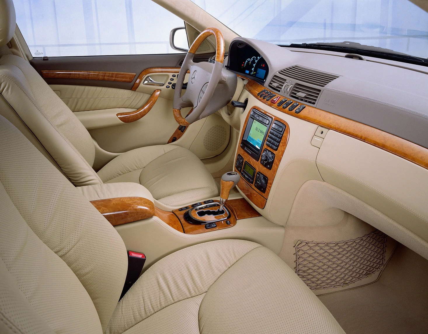 Innenraum eines Luxusautos mit beigen Ledersitzen, Holzelementen, Multifunktionslenkrad und modernem Armaturenbrett.
