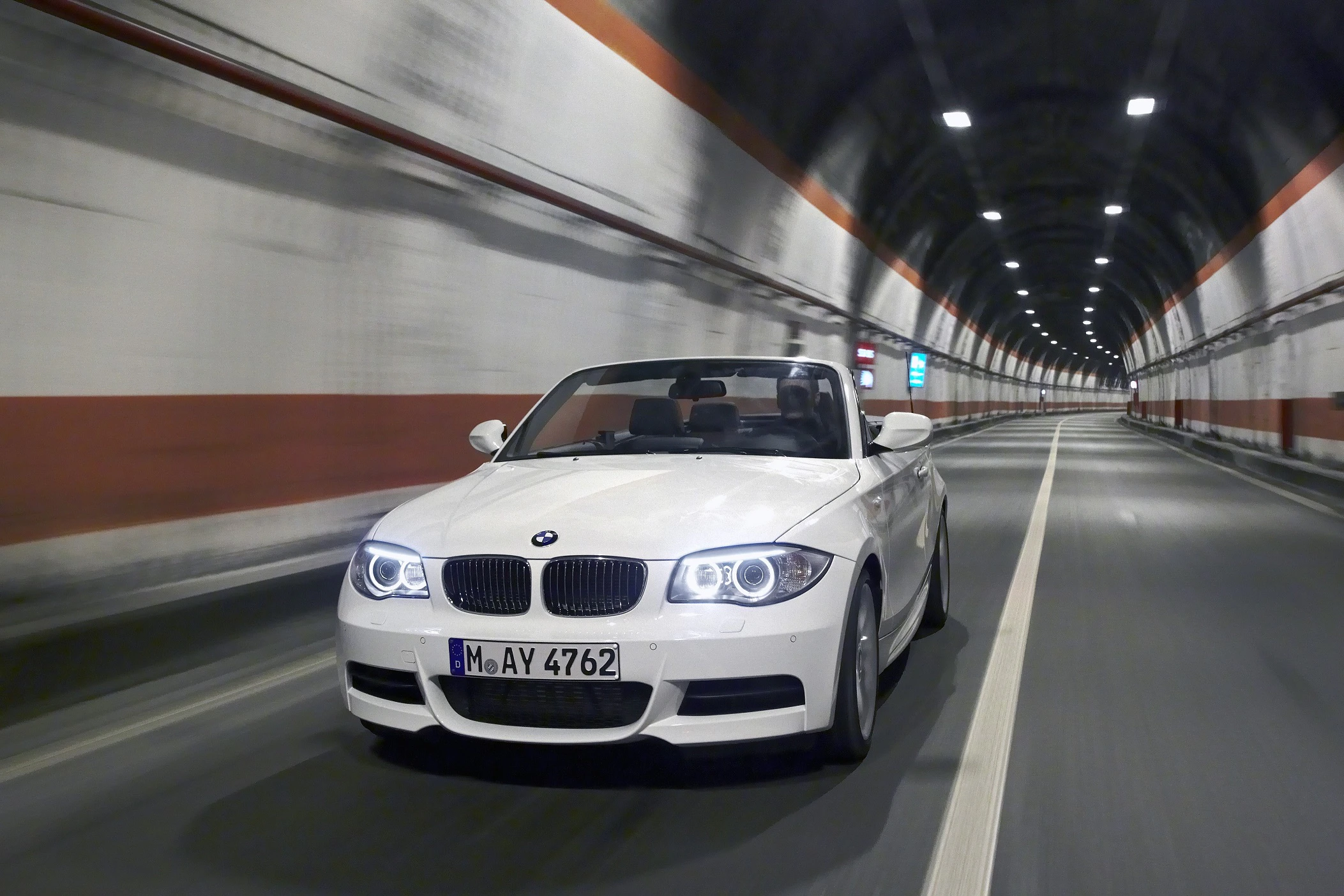 Weißes Cabrio fährt durch beleuchteten Tunnel. Dynamische Bewegung, Lichter an, keine Personen sichtbar.