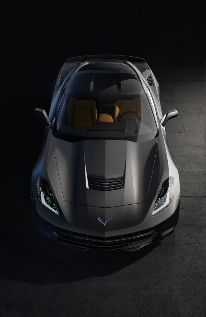 Silberner Sportwagen mit gelben Sitzen aus der Vogelperspektive, auf grauem Hintergrund, stark beleuchtet.