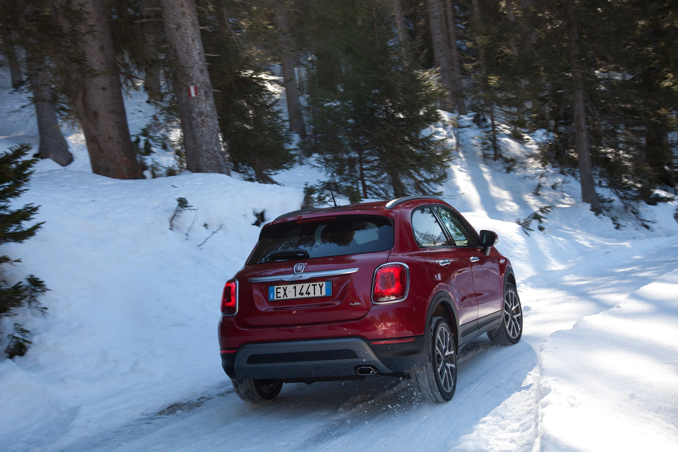 Rotes Auto fährt auf einer schneebedeckten Straße durch einen bewaldeten Winterlandschaft.