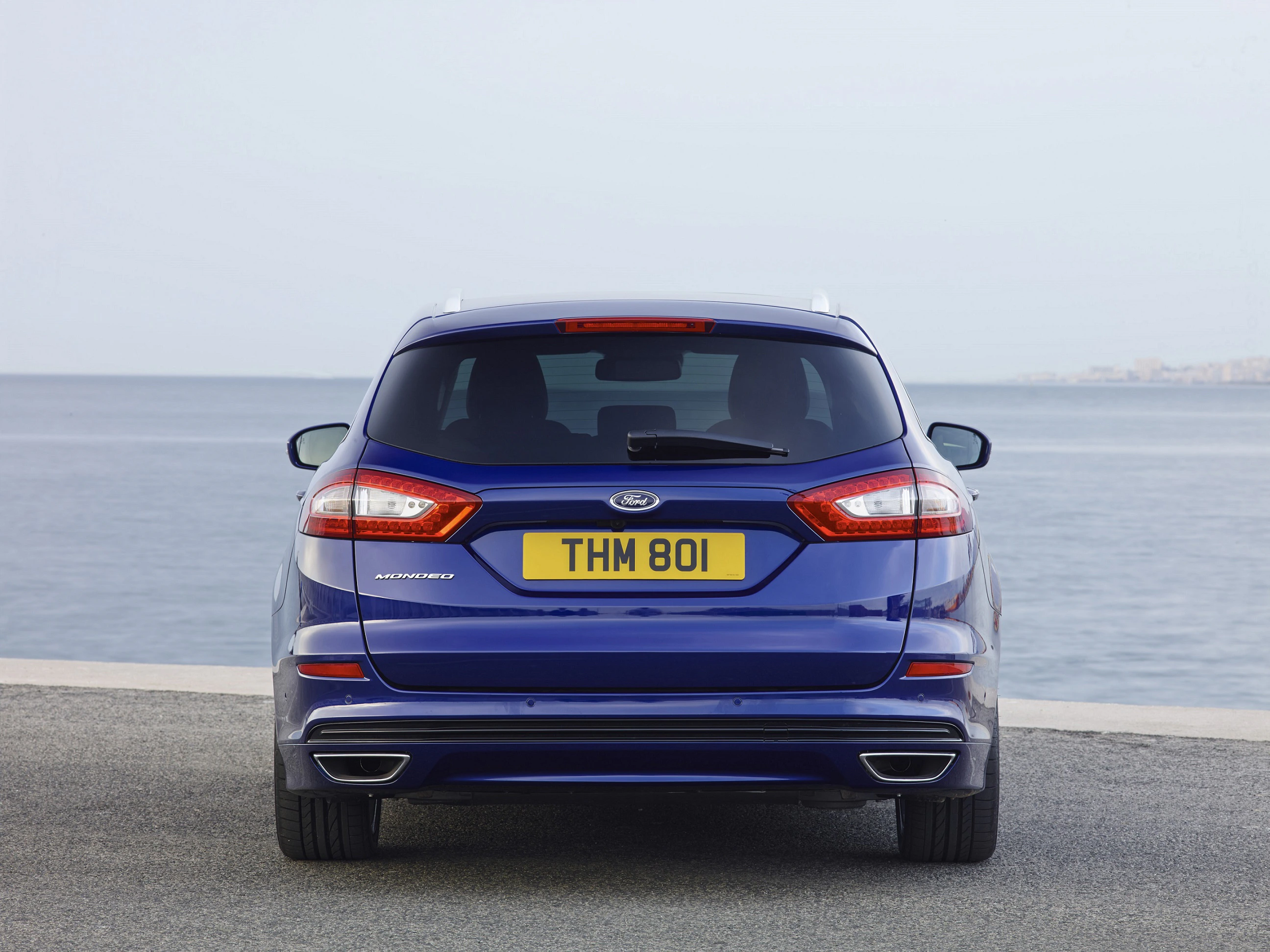 Blauer Ford Mondeo Kombi, Rückansicht, am Meer geparkt. Britisches Kennzeichen mit "THM 801". Ruhige, klare Küstenlandschaft im Hintergrund.