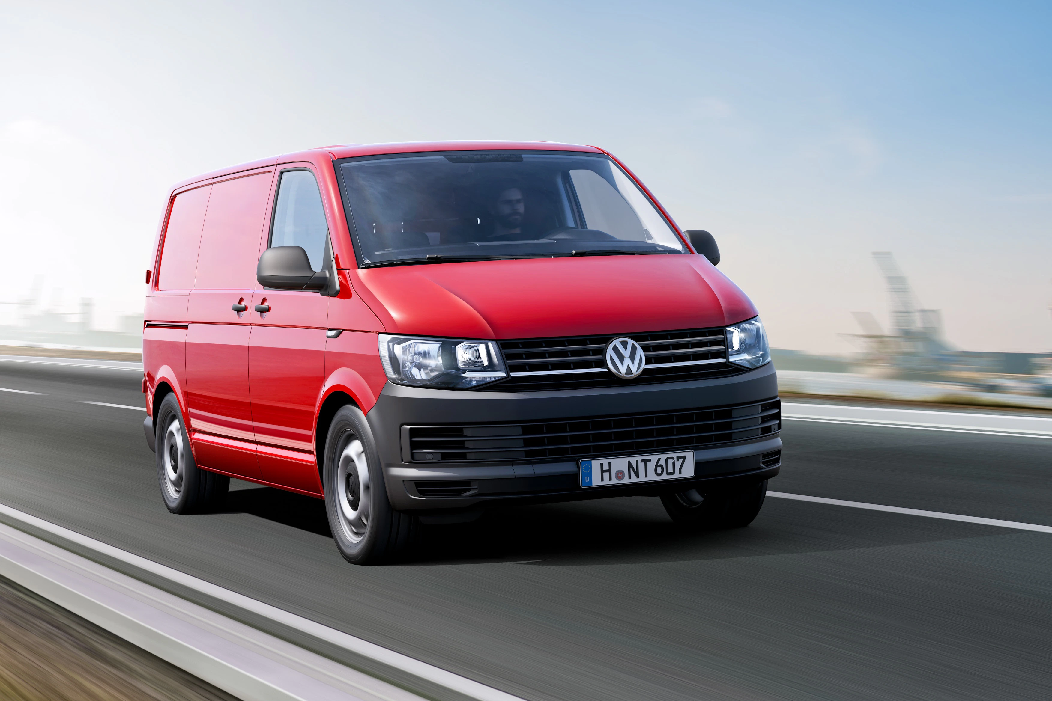 Roter Lieferwagen auf einer Autobahn, bewegt sich schnell in einer urbanen Umgebung bei klarem Himmel.