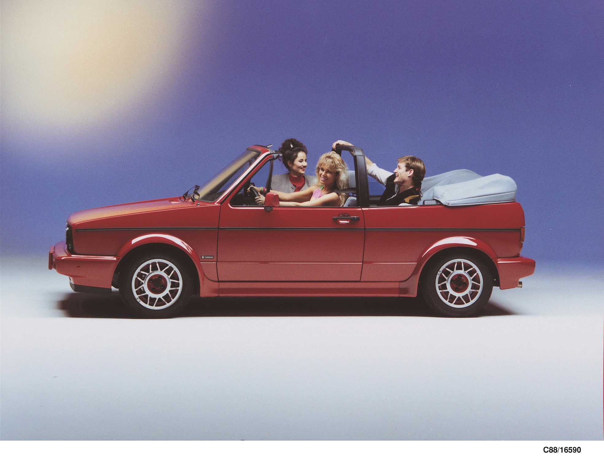 Rotes Cabrio mit vier lachenden Personen, offenem Verdeck, gestelltem Hintergrund und zwei Frauen sowie zwei Männern.