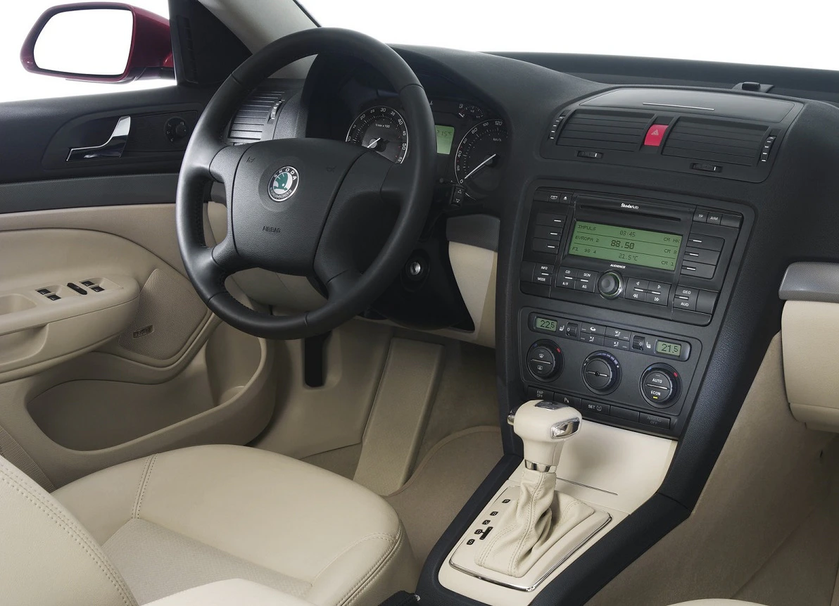 Innenraum eines Autos mit beigen Ledersitzen, schwarzem Multifunktionslenkrad und Mittelkonsole mit Anzeige und Bedienelementen.