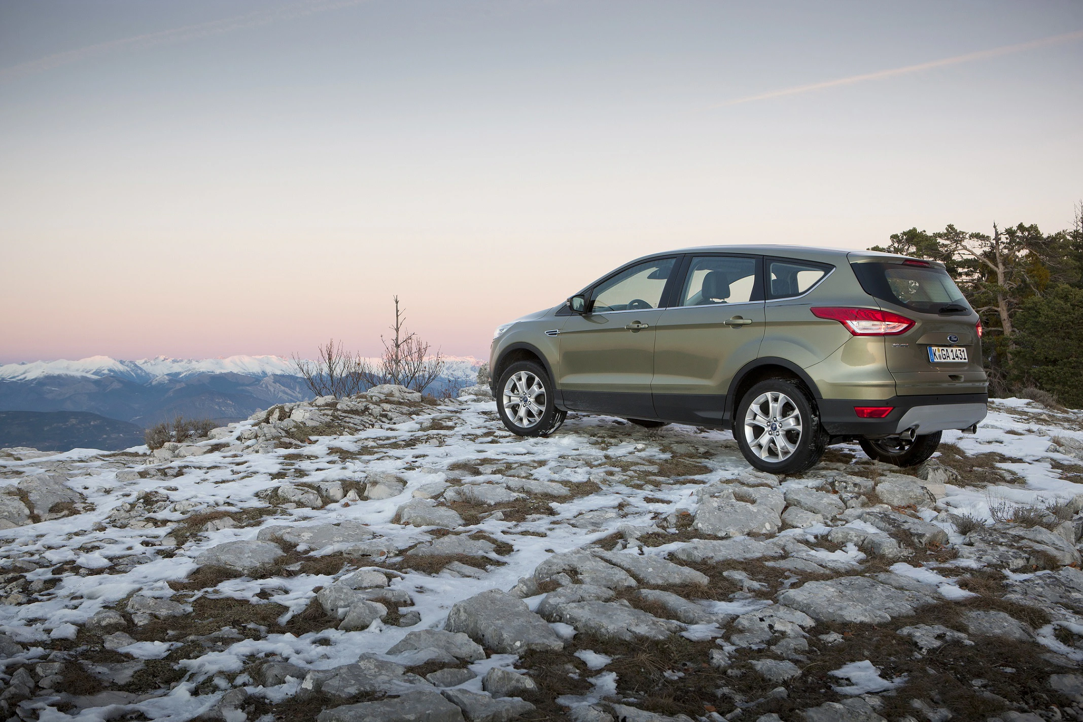 Ein SUV steht auf schneebedecktem, felsigem Gelände mit Blick auf ein winterliches, bergiges Panorama unter klarem Himmel.