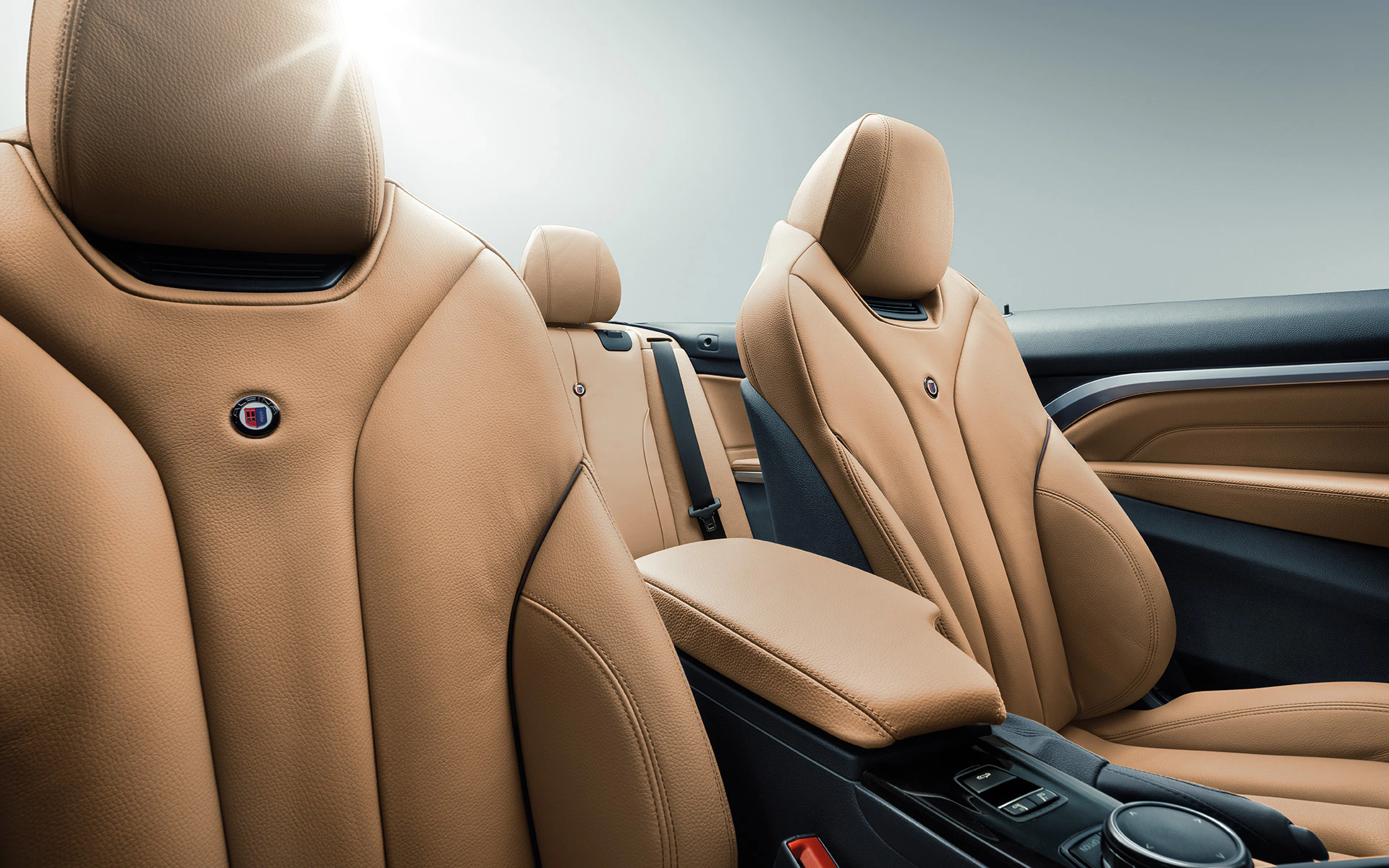 Braune Ledersitze eines Autos mit eleganten Nähten, Sonnenlicht im Hintergrund, Armlehne und Bedienelemente sichtbar.