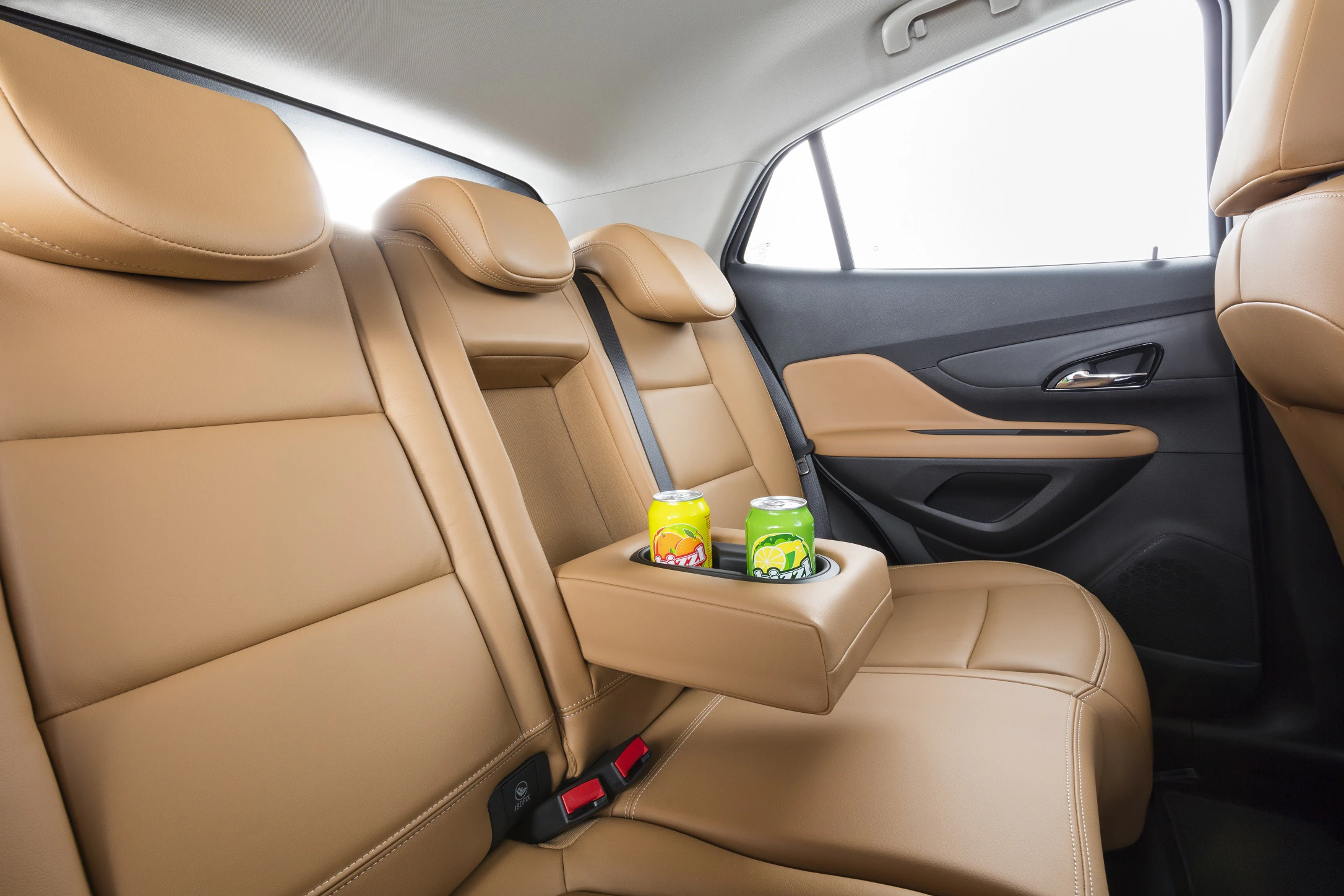 Rückbank eines Autos mit beigem Leder, heruntergeklappter Mittelarmlehne und zwei Getränkedosen darauf.