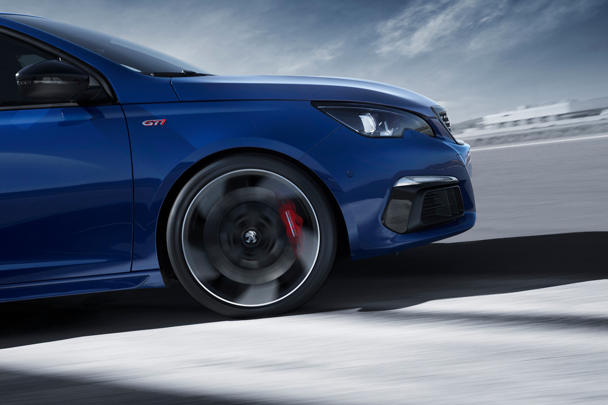 Blauer Sportwagen in Bewegung, seitliche Nahaufnahme des Vorderrads auf Asphaltstraße vor unscharfem Hintergrund.