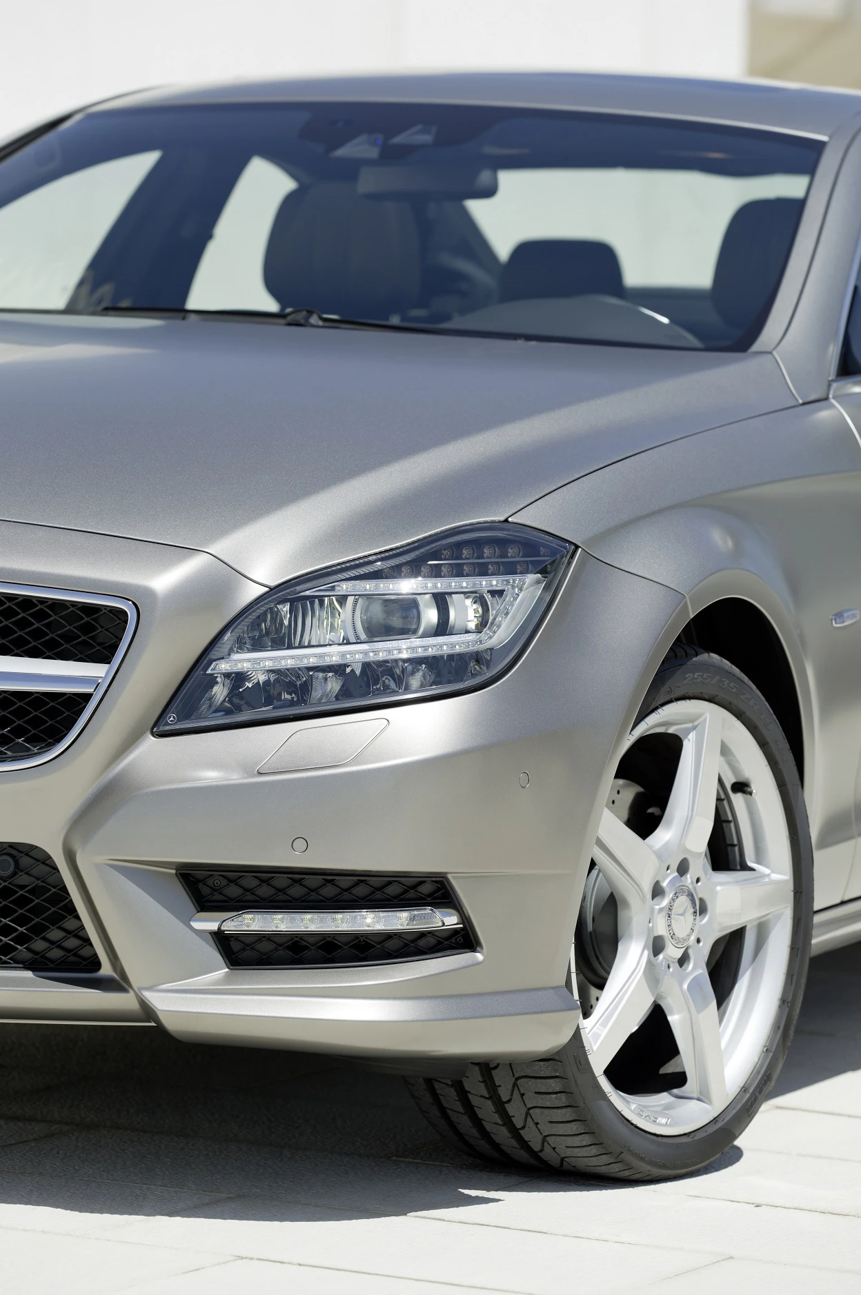 Vorderansicht eines silbernen Luxusautos mit sportlichem Design und markanten Scheinwerfern, geparkt auf hellem Pflaster.