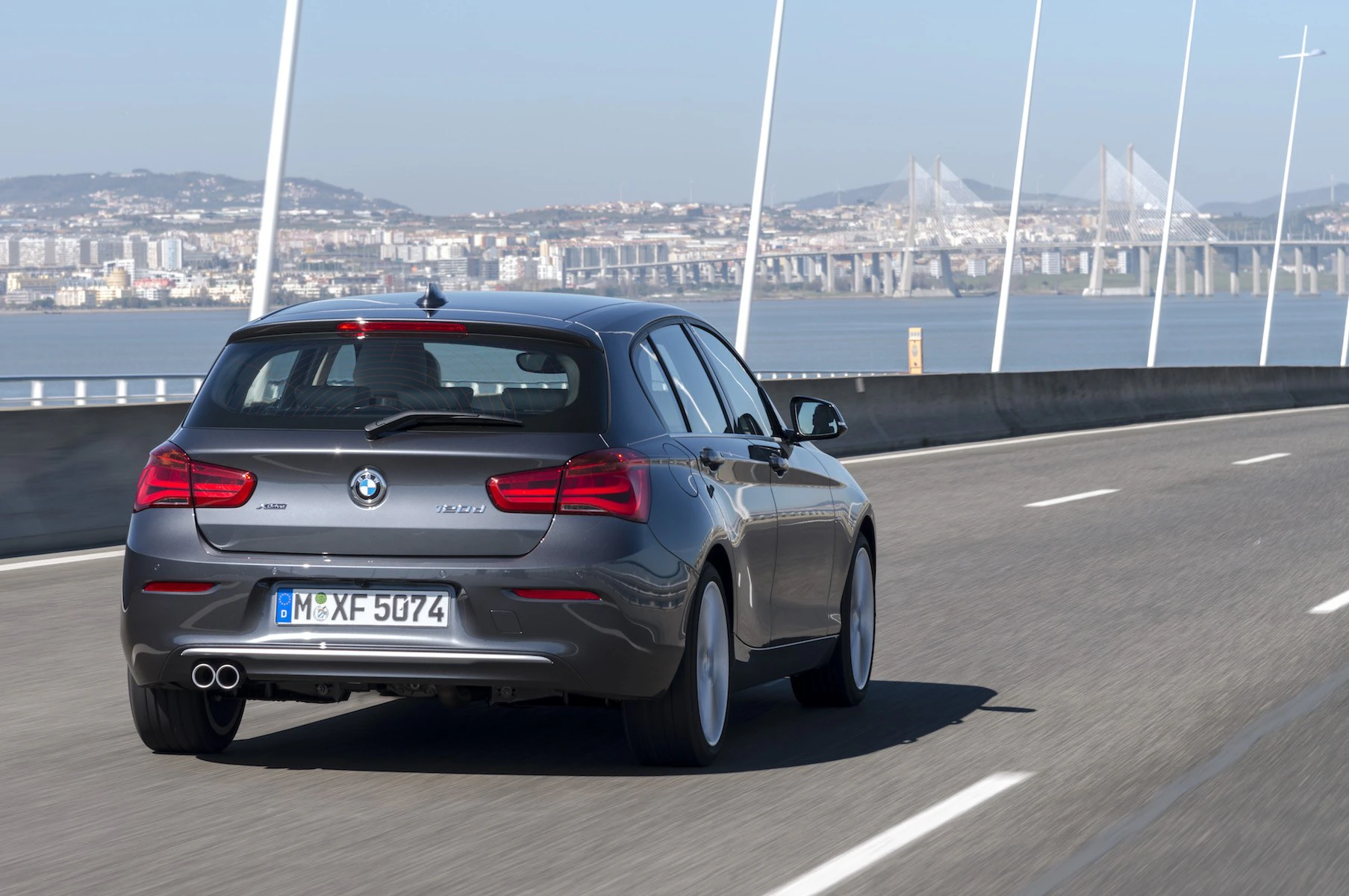 Ein grauer BMW fährt auf einer Brücke mit Blick auf eine Stadt im Hintergrund.