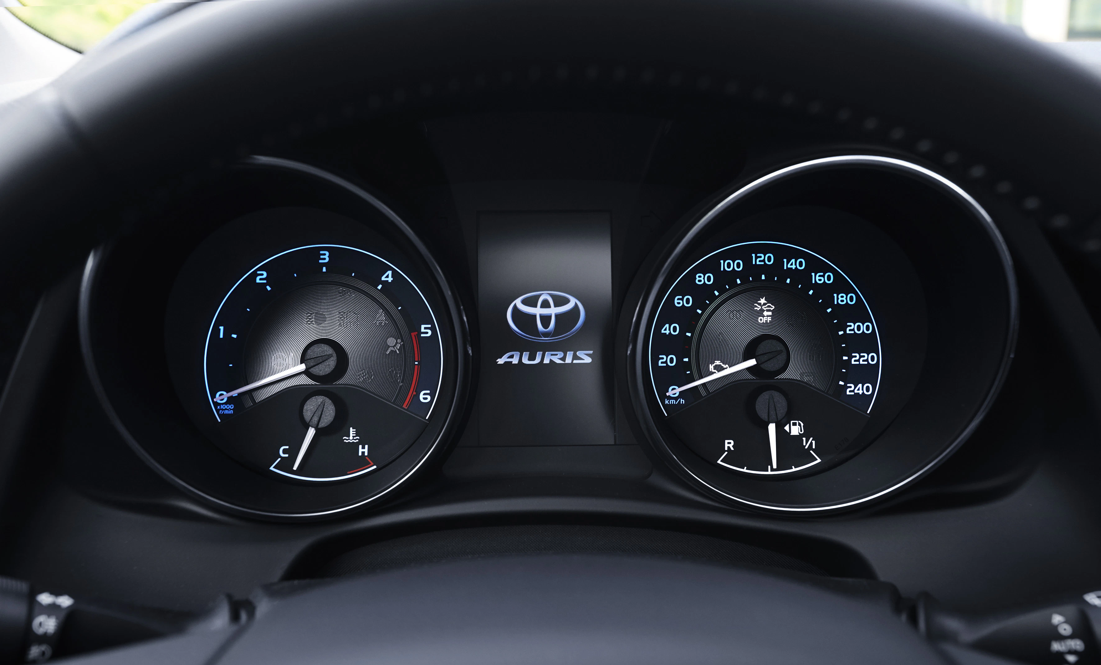 Armaturenbrett eines Toyota Auris mit Tachometer und Drehzahlmesser, beide in Blau und Schwarz. Logo und Schriftzug in der Mitte.