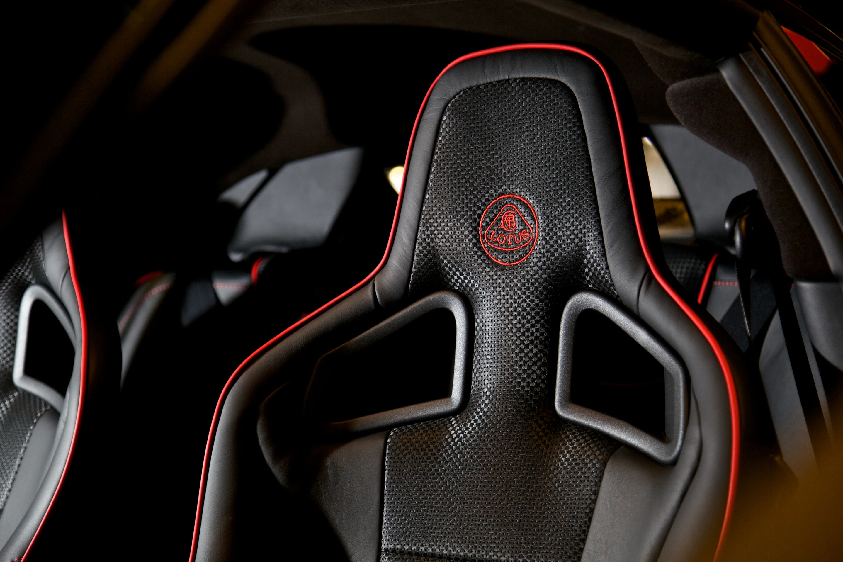 Nahaufnahme eines Autositzes aus schwarzem Leder mit roten Nähten und einem Lotus-Logo, das eine stilvolle und sportliche Optik verleiht.