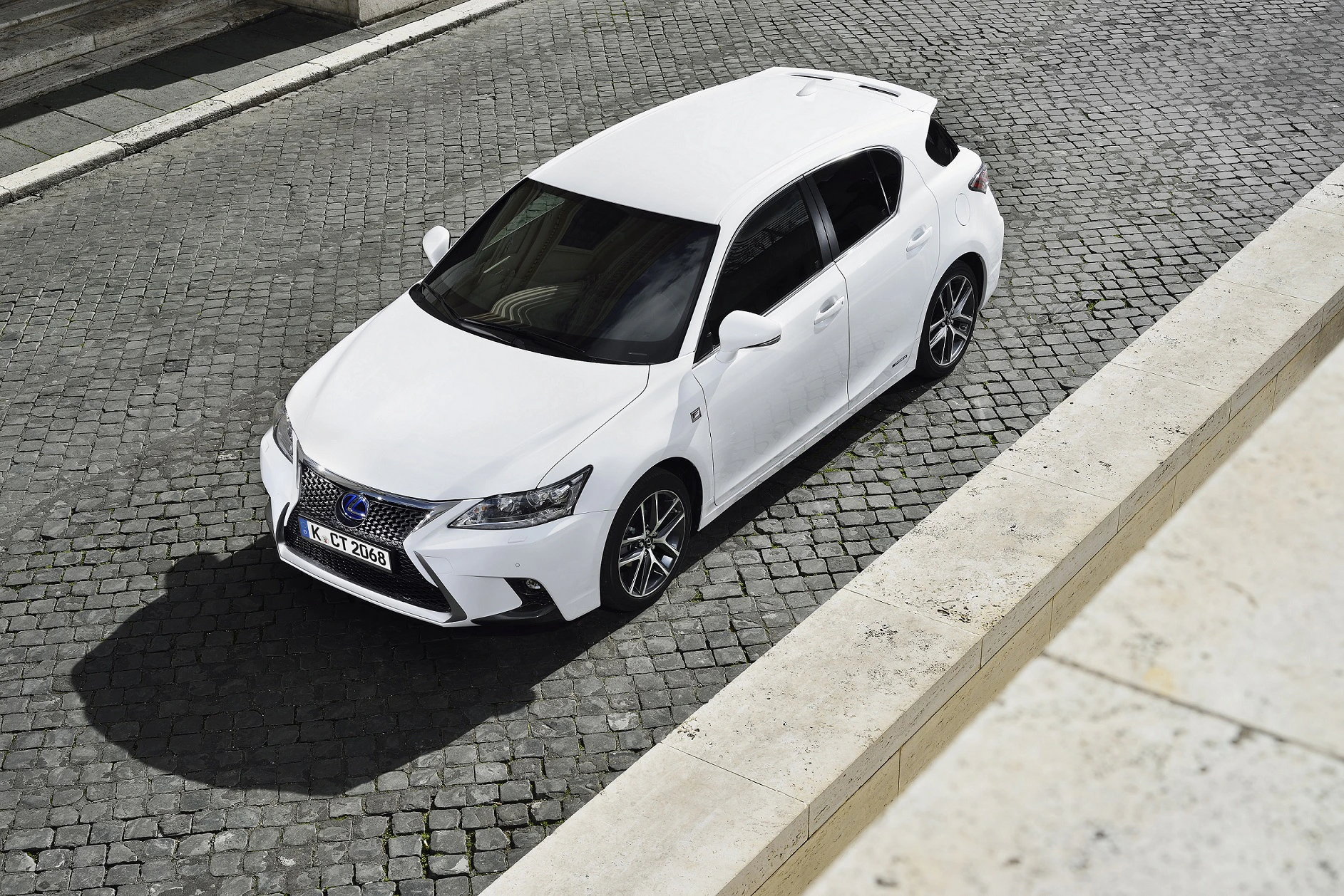 Weißer Lexus CT, von oben fotografiert, steht auf einer gepflasterten Straße in einer urbanen Umgebung.