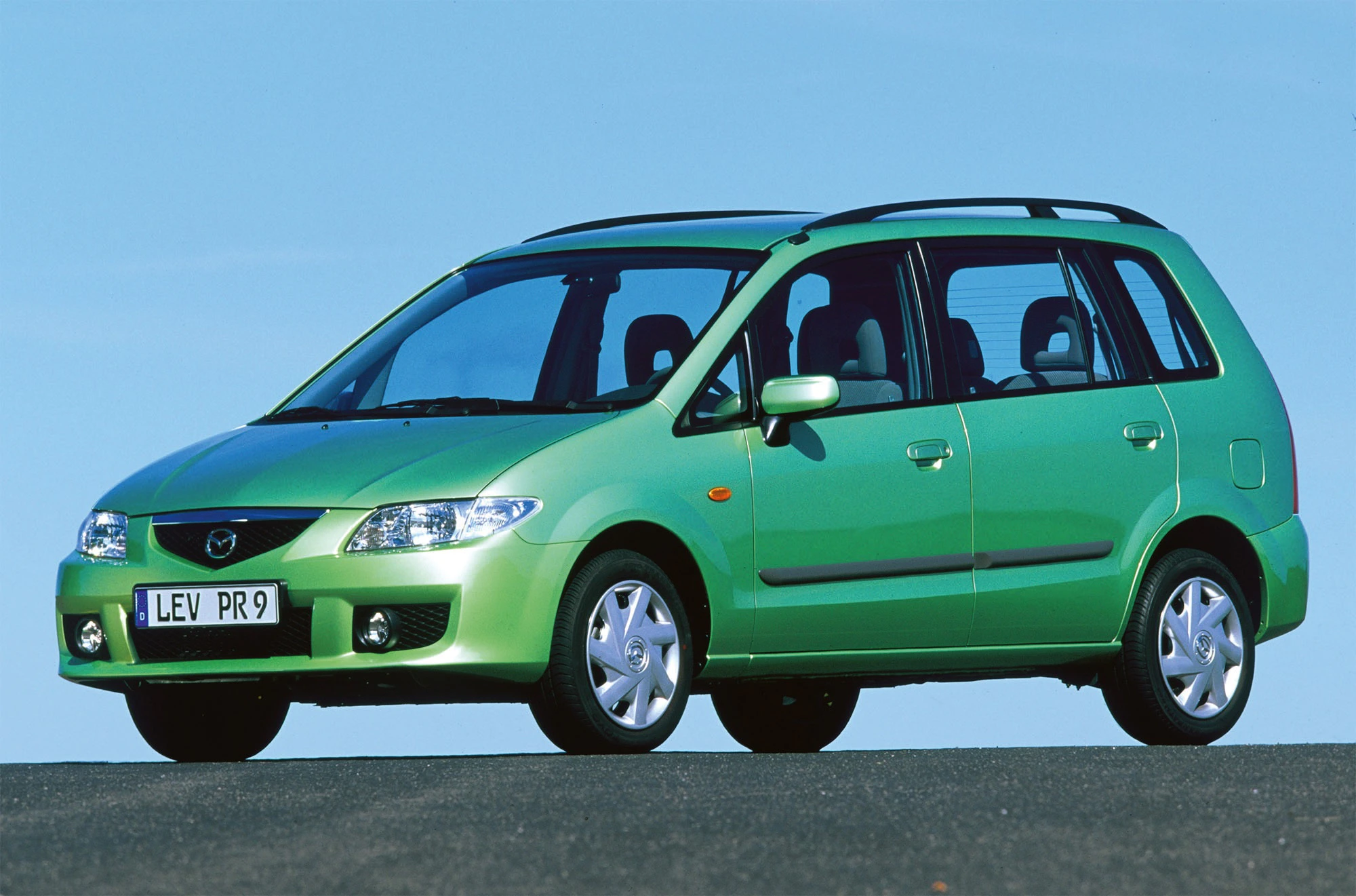 Grünes Auto, wahrscheinlich ein älterer Minivan-Modell, auf einer Straße vor klarem, blauen Himmel geparkt.