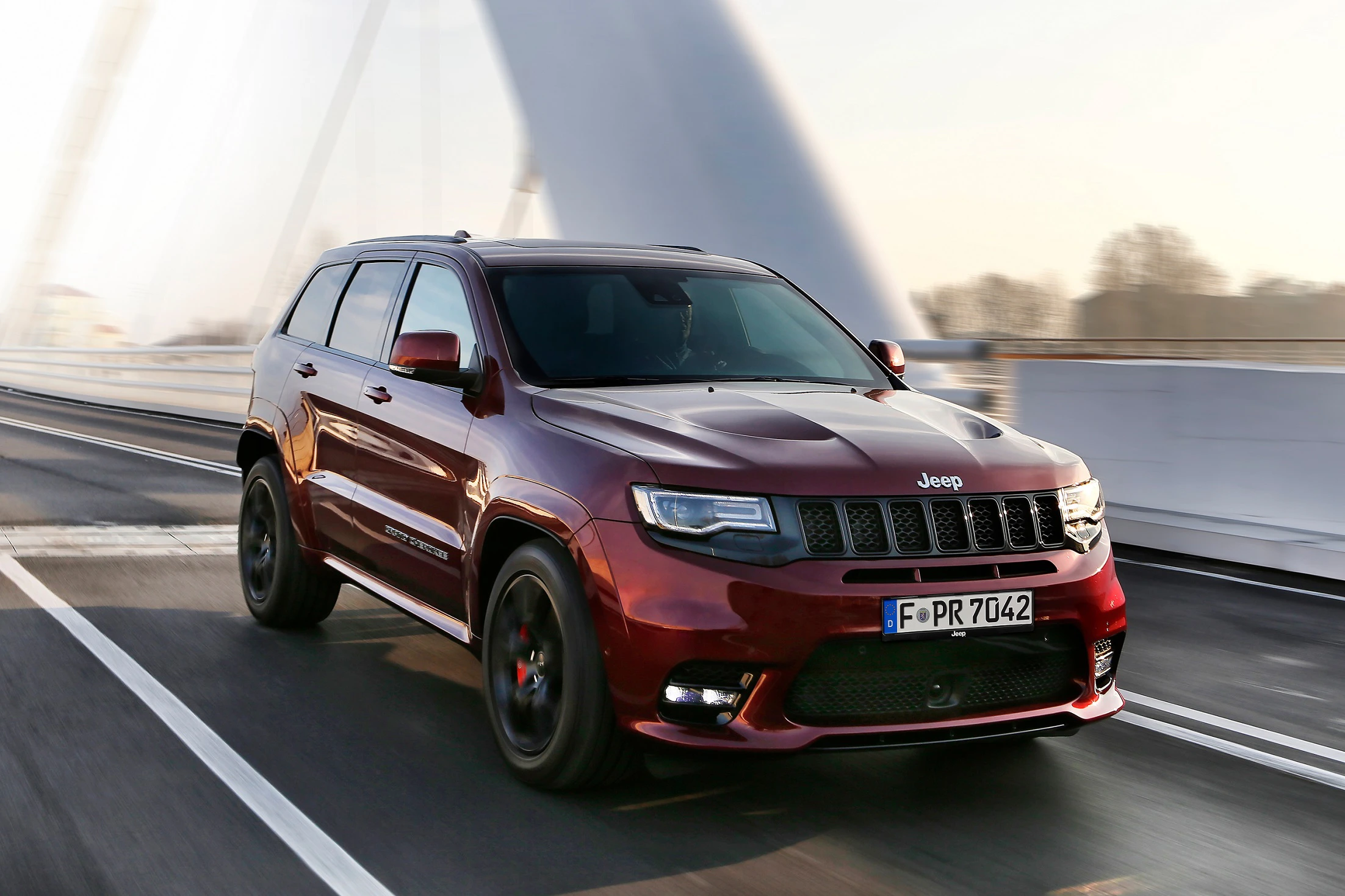 Roter Jeep SUV fährt über eine Brücke bei Tageslicht. Der Wagen hat schwarz getönte Fenster und eine deutsche Nummerntafel.
