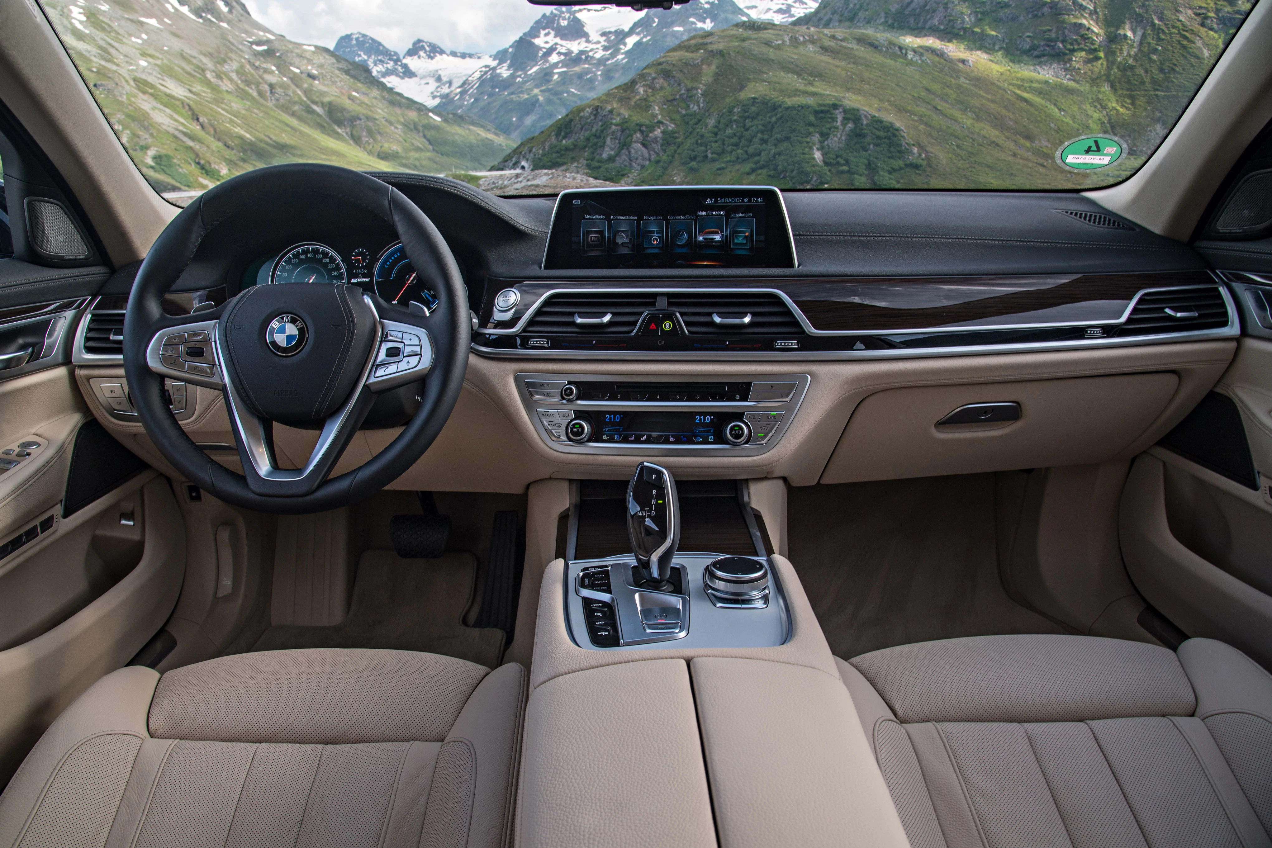 Innenraum eines BMWs mit beigem Leder, modernem Armaturenbrett und Landschaftsansicht durch die Windschutzscheibe.