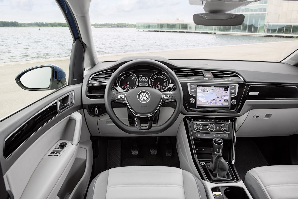 Lenkrad und Armaturenbrett eines VW-Autos mit eingebautem Navigationssystem. Blick aus dem Innenraum auf eine Wasserlandschaft.