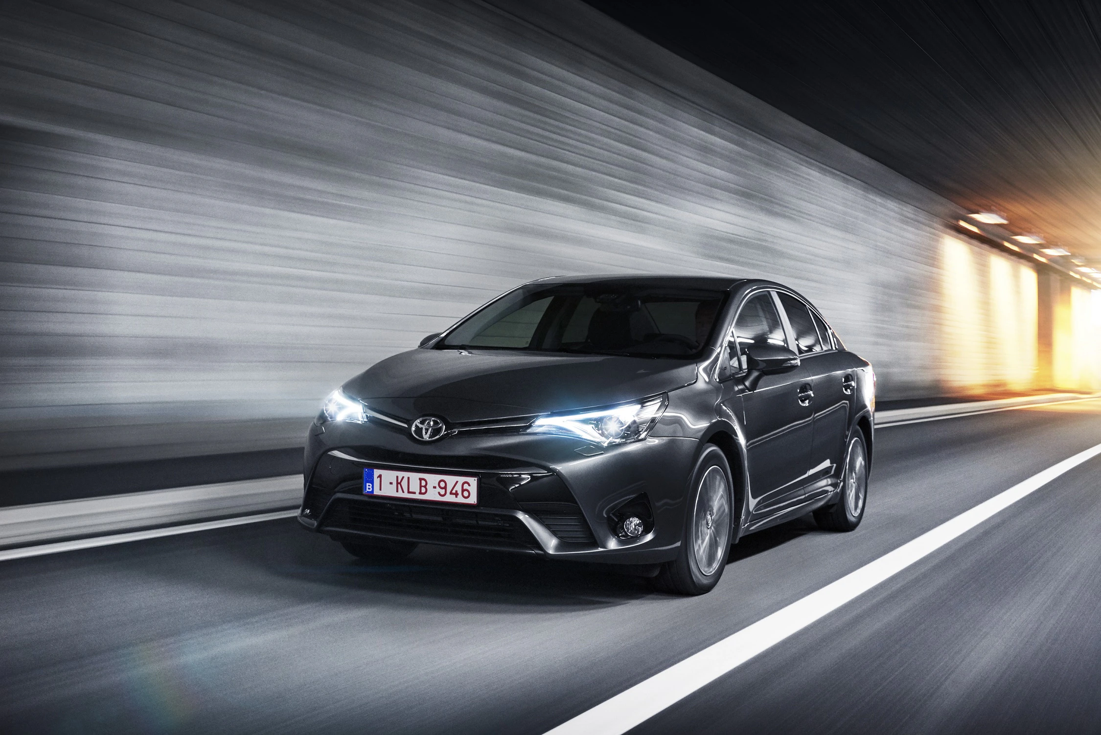 Schwarzer Toyota fährt durch einen beleuchteten Tunnel. Dynamische Perspektive, seitlicher Blick auf das Fahrzeug auf der Straße.