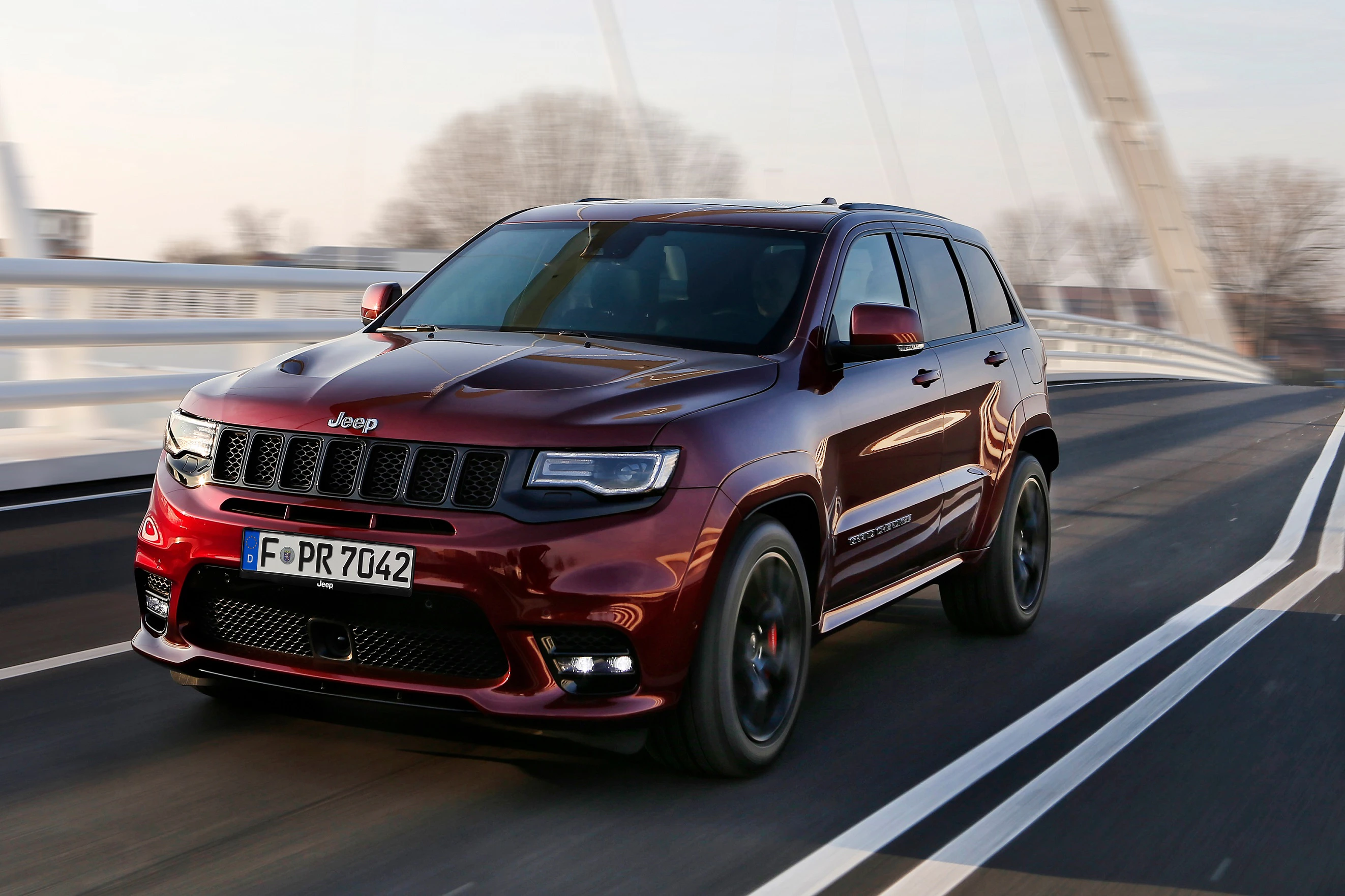 Roter SUV fährt über eine Brücke bei Tageslicht. Fahrzeug ist ein Jeep mit deutscher Zulassung.