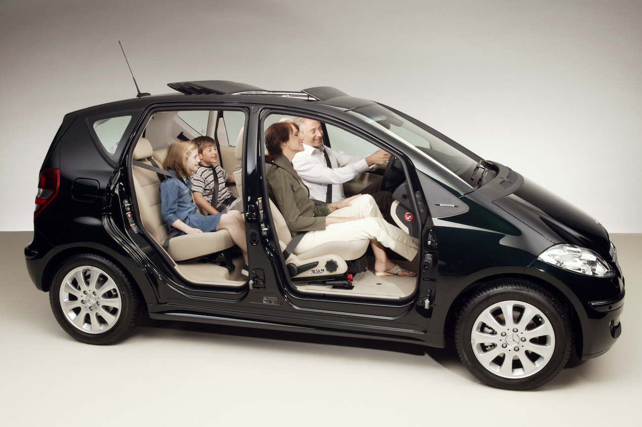 Schwarzes Auto mit geöffneten Türen, eine Familie mit zwei Erwachsenen und zwei Kindern sitzt darin und wirkt zufrieden.