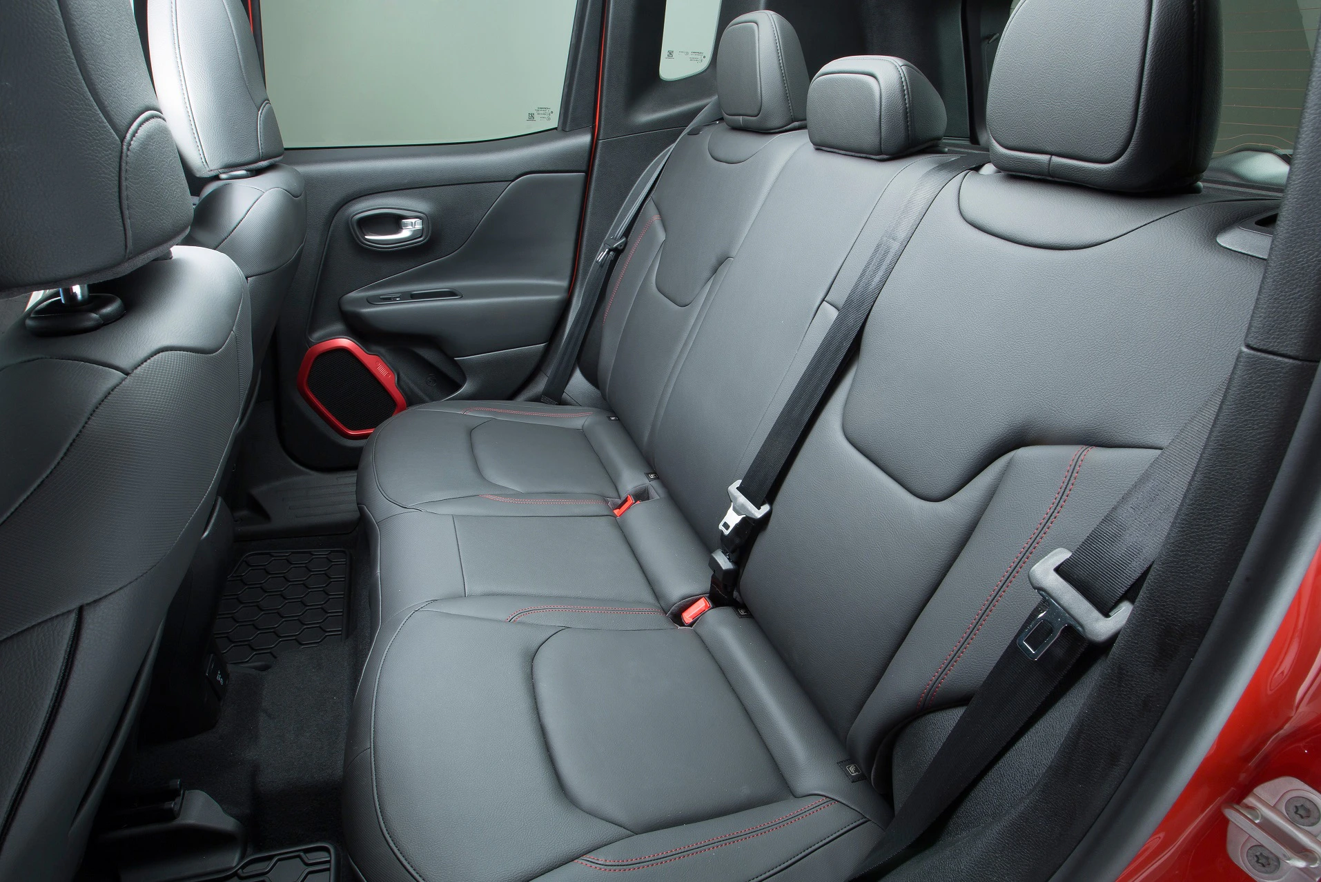Rückbank eines Autos mit schwarzer Lederausstattung und roten Nähten. Sicherheitsgurte und Autotüren im Hintergrund sichtbar.