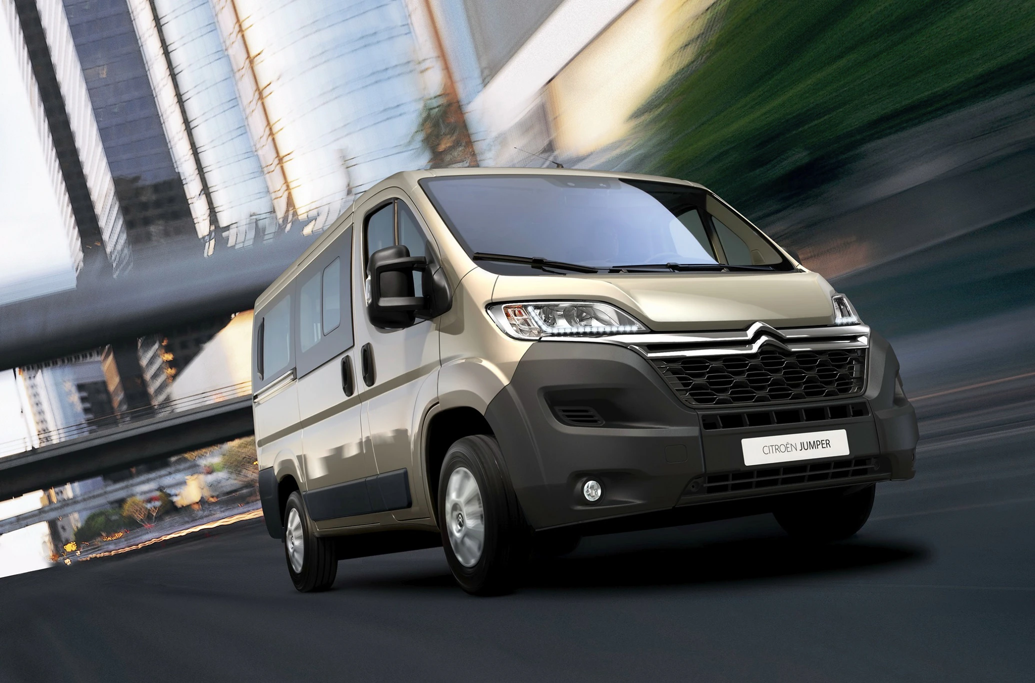 Silberner Citroën Jumpy fährt dynamisch durch eine städtische Kulisse mit Hochhäusern im Hintergrund.