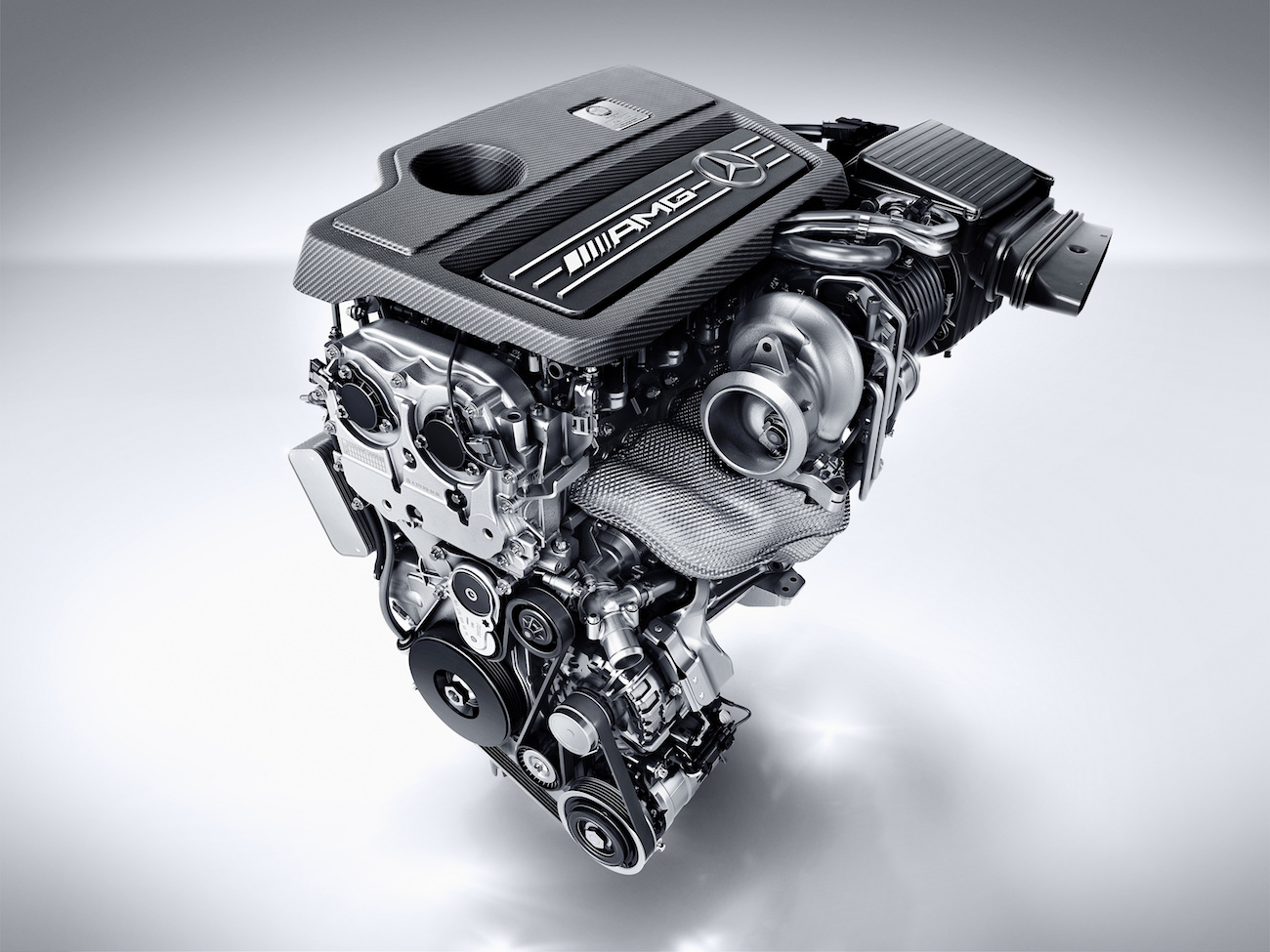 Ein moderner AMG-Automotor mit sichtbaren Komponenten wie Turbolader, Riemen und hochwertigen Metallteilen, auf grauem Hintergrund.