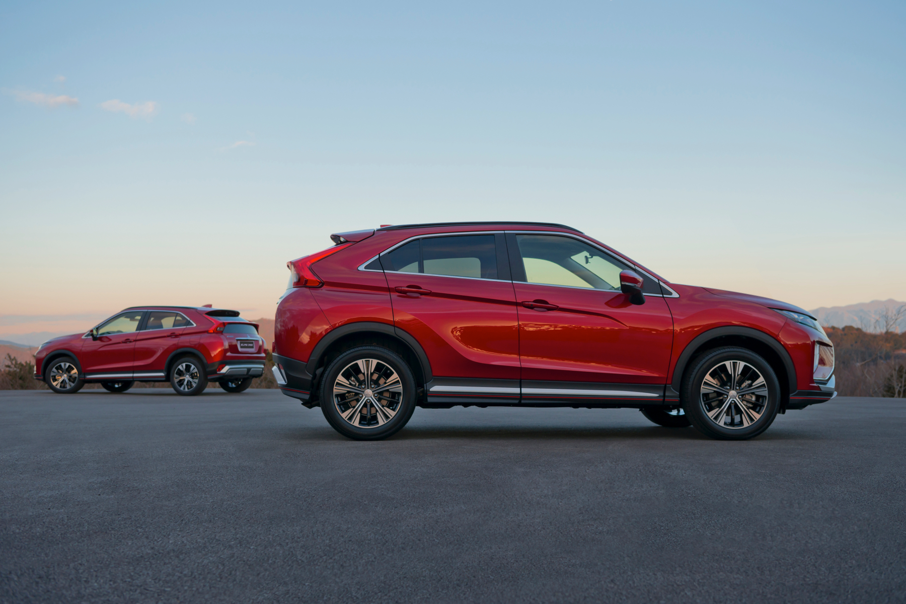 Zwei rote Crossover-SUVs parken nebeneinander auf einer offenen Fläche bei Sonnenuntergang, mit Bergen im Hintergrund.