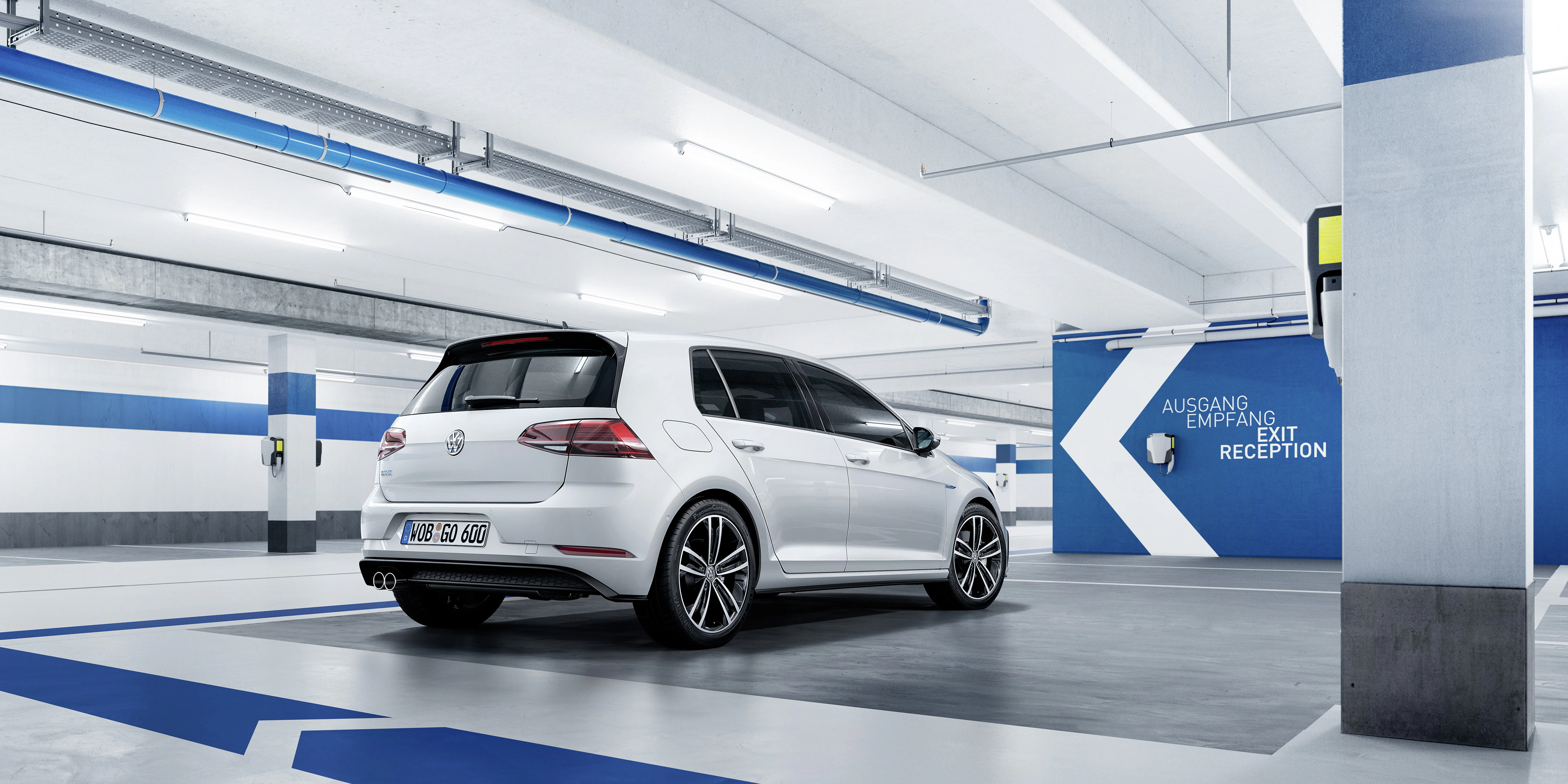 Ein weißer VW Golf in einem modernen, hell beleuchteten Parkhaus. Markierungen für Ausgang und Empfang sind an der Wand sichtbar.
