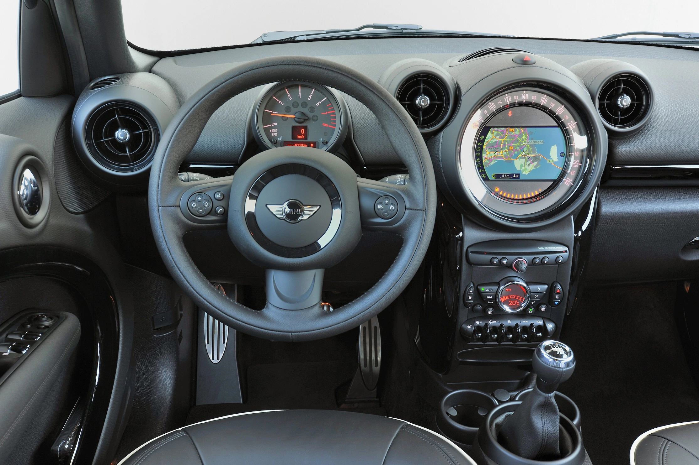 Innenraum eines Autos mit Lenkrad, Armaturenbrett und Navigationssystem. Zwei Rundanzeigen und ein Schalthebel sind ebenfalls sichtbar.