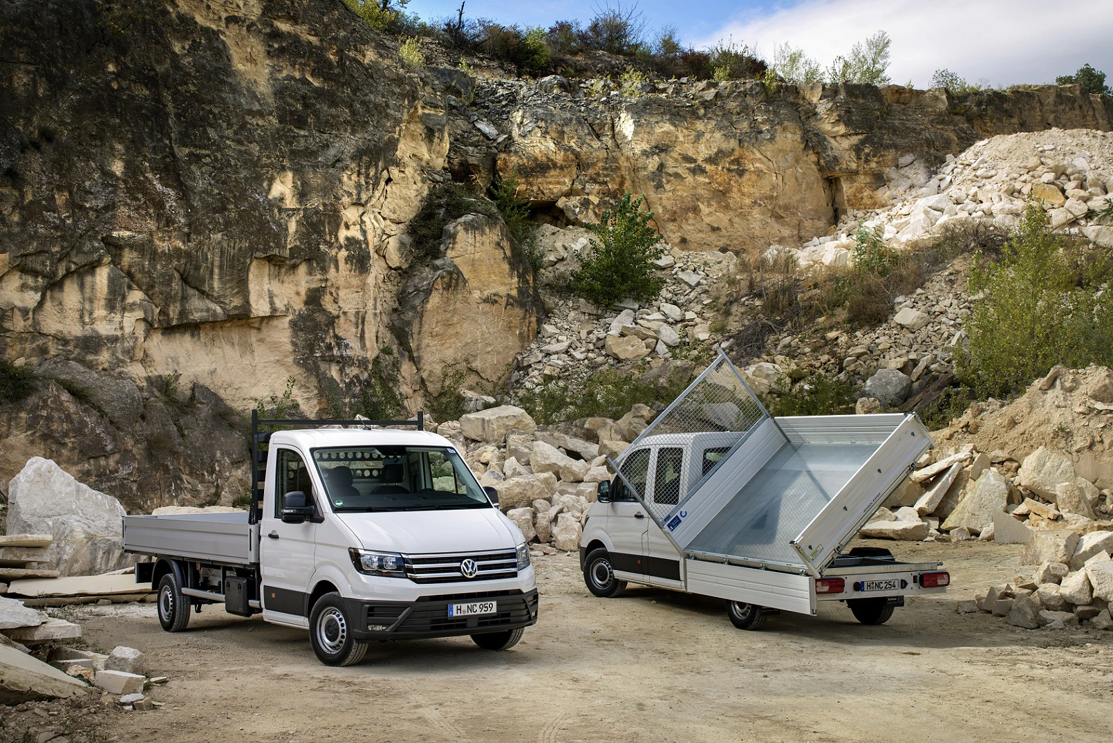 Zwei weiße Kleintransporter in einem Steinbruch; einer hat eine gekippte Ladefläche. Felswände und Geröll im Hintergrund.