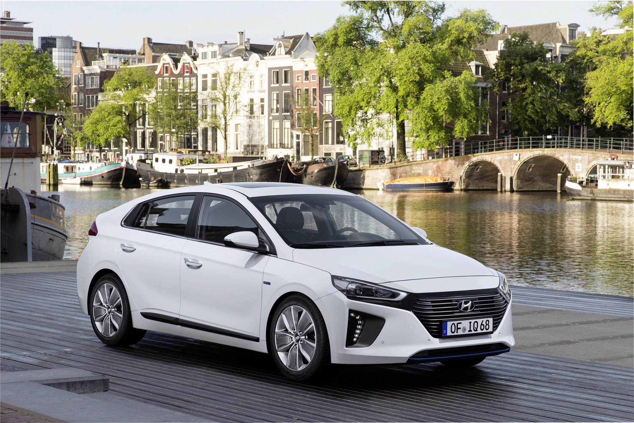 Ein weißer Hyundai steht auf einem Steg vor einer malerischen Stadtkulisse mit Kanälen und Backsteinhäusern.