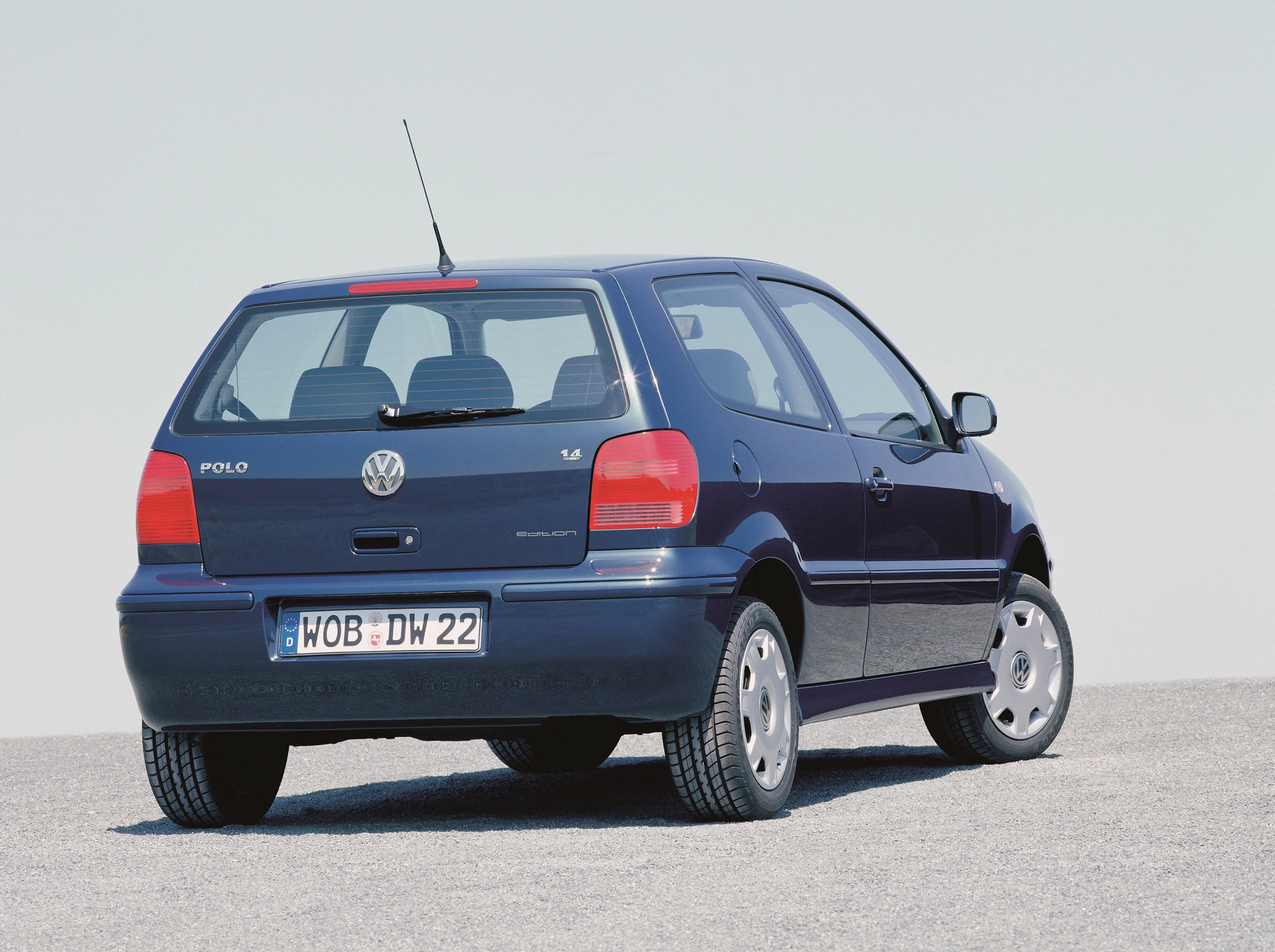 Blauer Volkswagen Polo 1.4, Rückansicht, auf einem asphaltierten Platz. Himmel im Hintergrund.