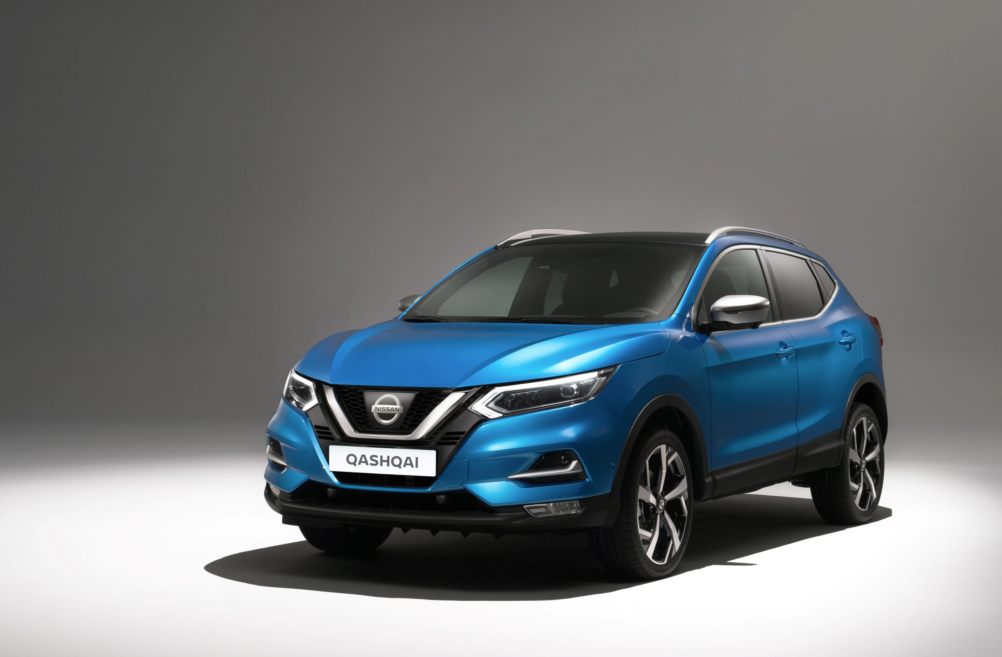 Blauer Nissan Qashqai SUV auf grauem Hintergrund, von vorne schräg fotografiert, mit modernen Scheinwerfern und markantem Markenlogo.